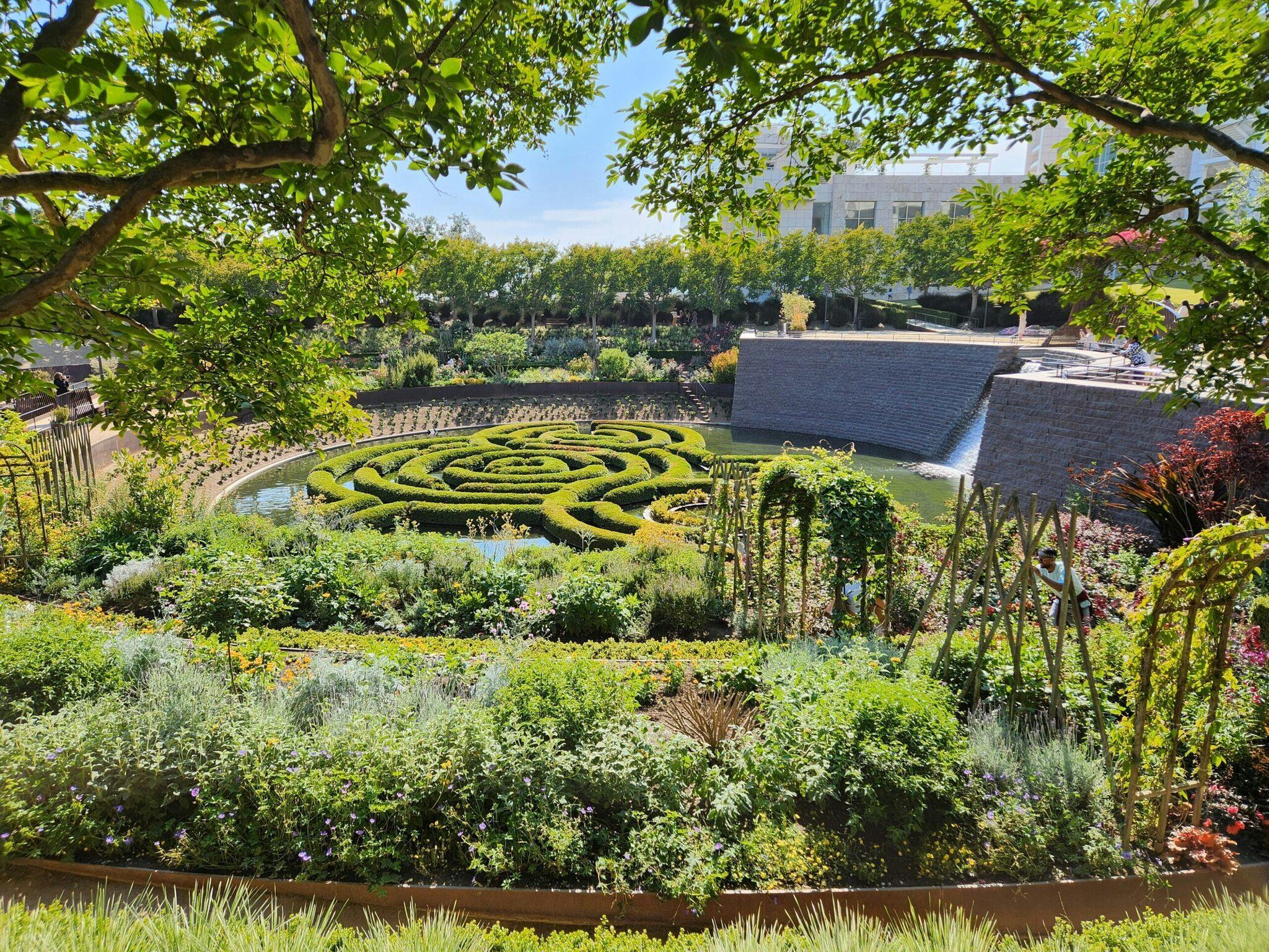 Un jardin à la française avec un parterre de buis en spirale, bassin et bâtiment en pierre en arrière-plan