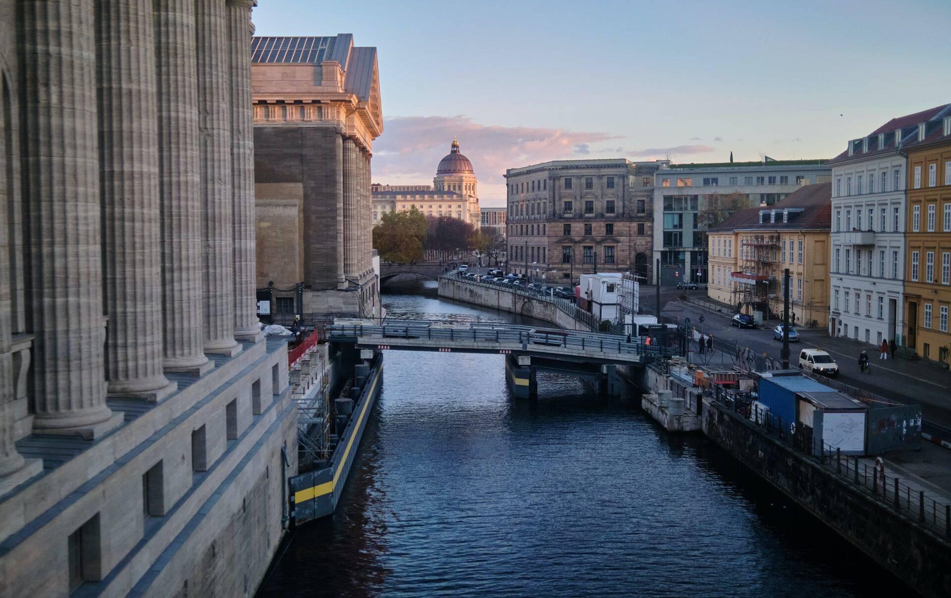 Vue sur un canal urbain avec ponts, bâtiments historiques et un dôme architectural en arrière-plan