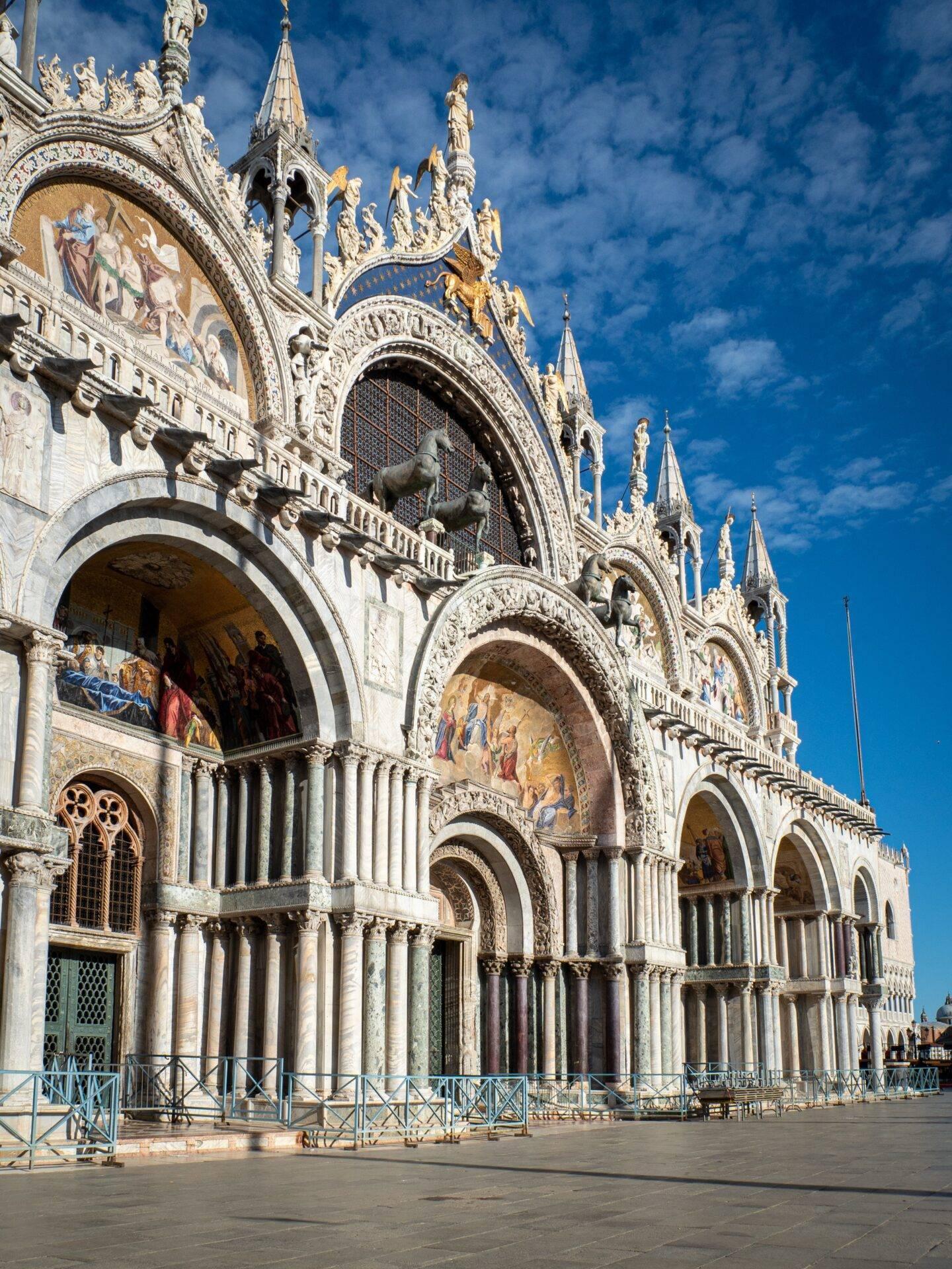 Façade ornée d’une basilique vénitienne avec arcades gothiques, sculptures dorées et mosaïques sous ciel bleu