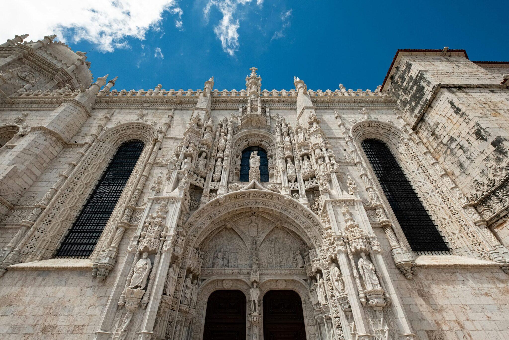 Façade ornementée d’une église gothique en pierre blanche avec portail central richement sculpté et rosaces