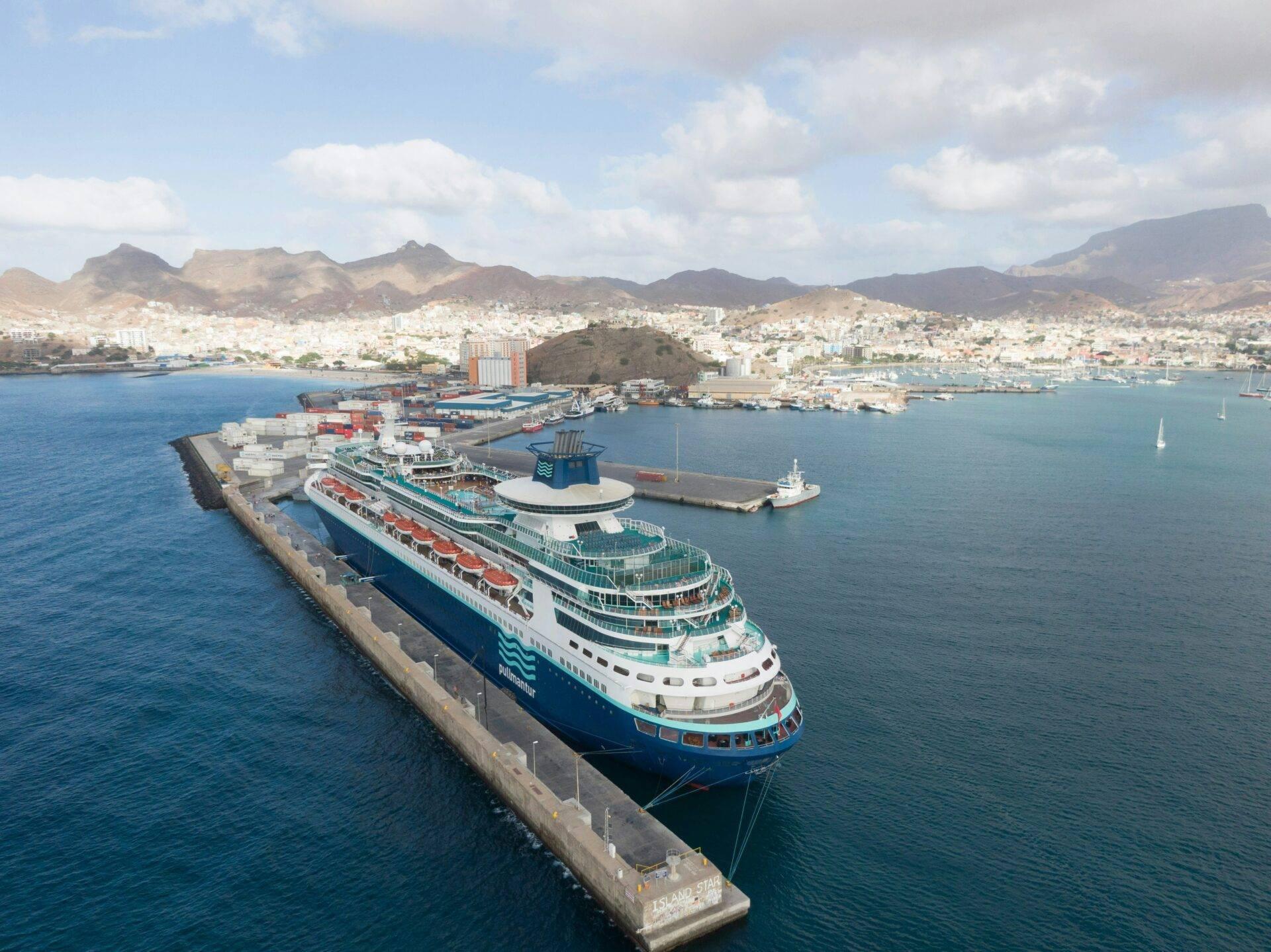 Un grand navire de croisière amarré au port d’une ville côtière méditerranéenne avec montagnes arides en arrière-plan