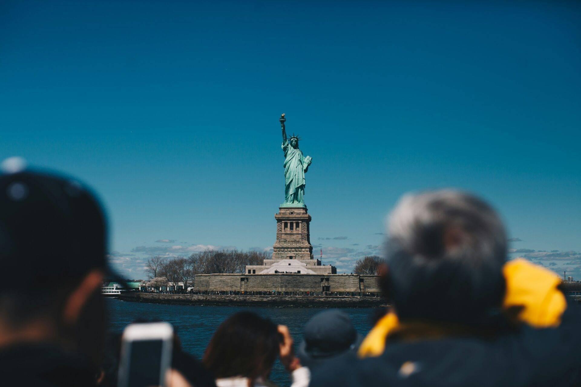 Des touristes photographient une statue iconique de la liberté sur son île, sous un ciel bleu dégagé