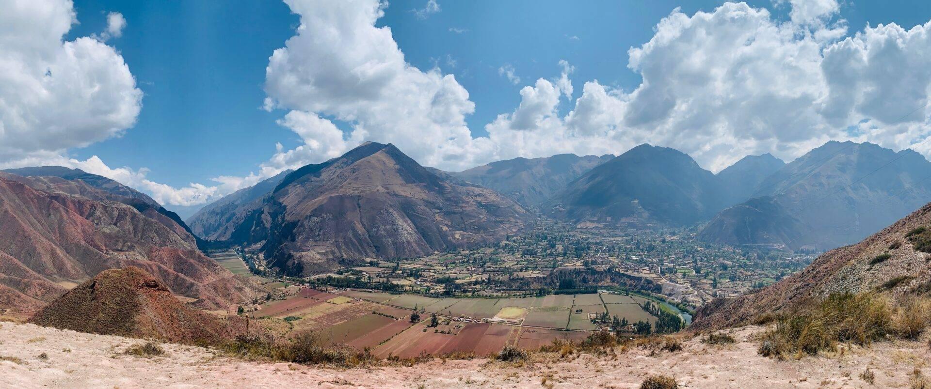 Vallée andine avec montagnes escarpées, champs cultivés en terrasses, rivière sinueuse et villages dispersés sous ciel nuageux