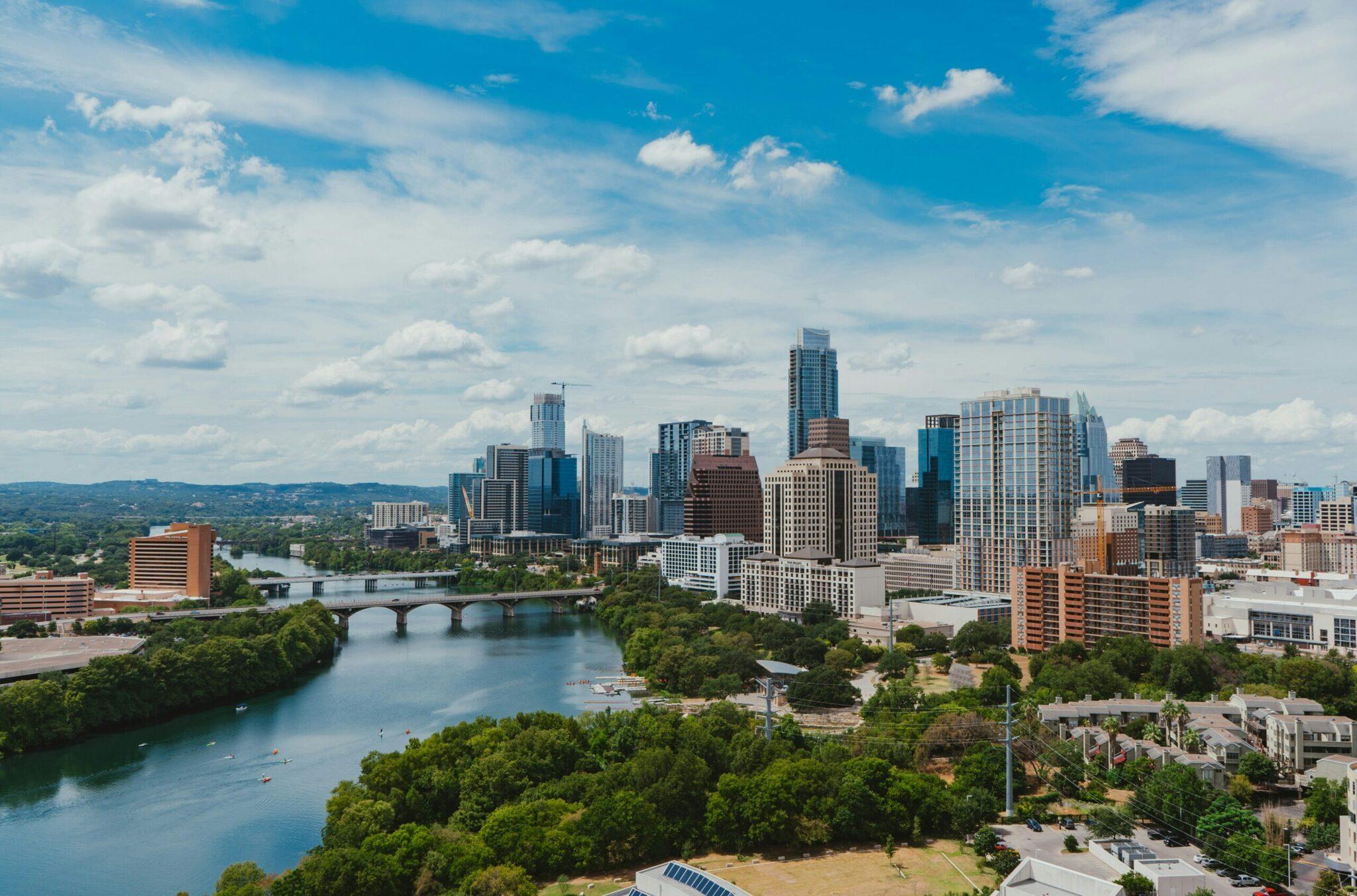 Vue panoramique d’une skyline urbaine avec gratte-ciel, rivière et collines verdoyantes sous ciel bleu nuageux