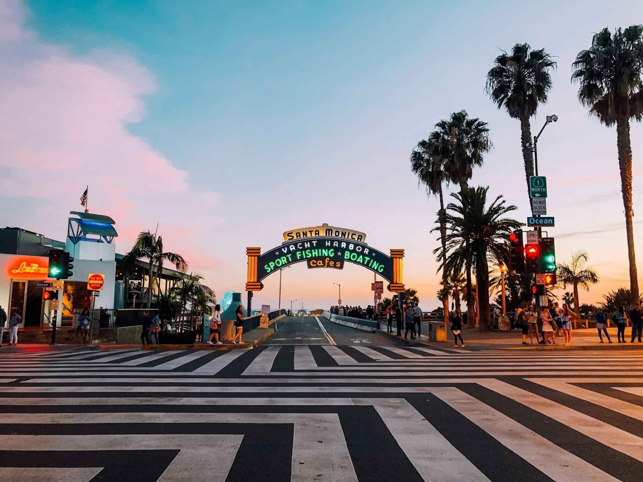 L’emblématique arche de Santa Monica Yacht Harbor au coucher de soleil avec palmiers et passage pour piétons