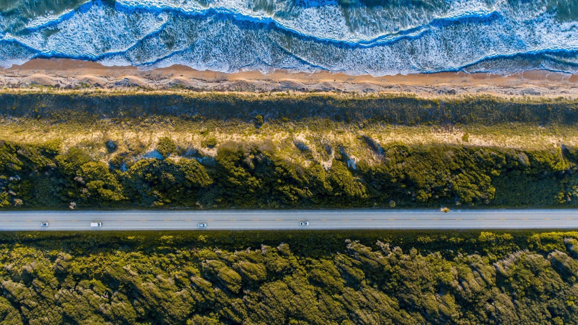 Vue aérienne d’une route côtière traversant une forêt luxuriante avec plage et vagues de l’océan Indien