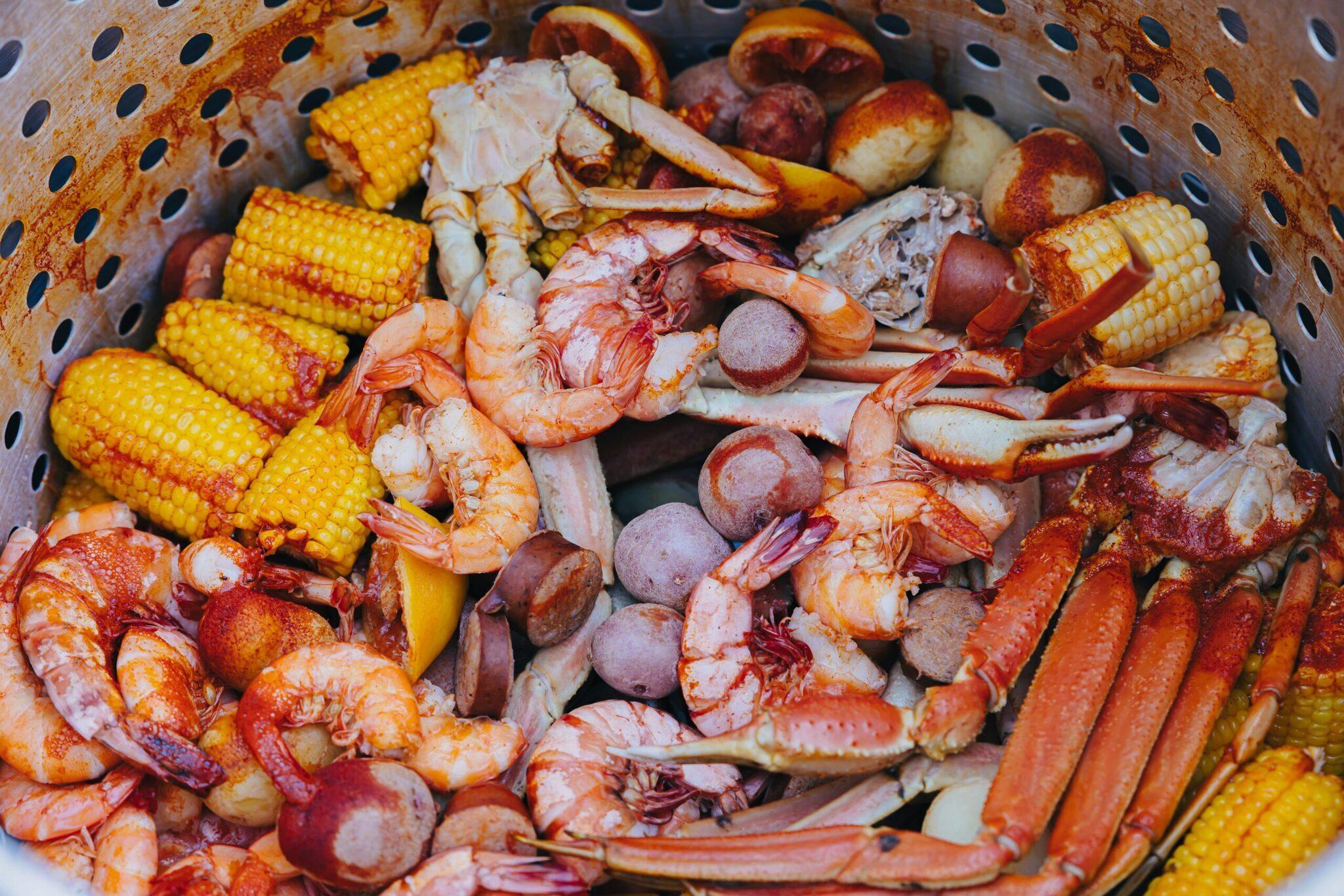 Un panier perforé rempli de fruits de mer cuits incluant crevettes, crabe, saucisses et maïs grillé