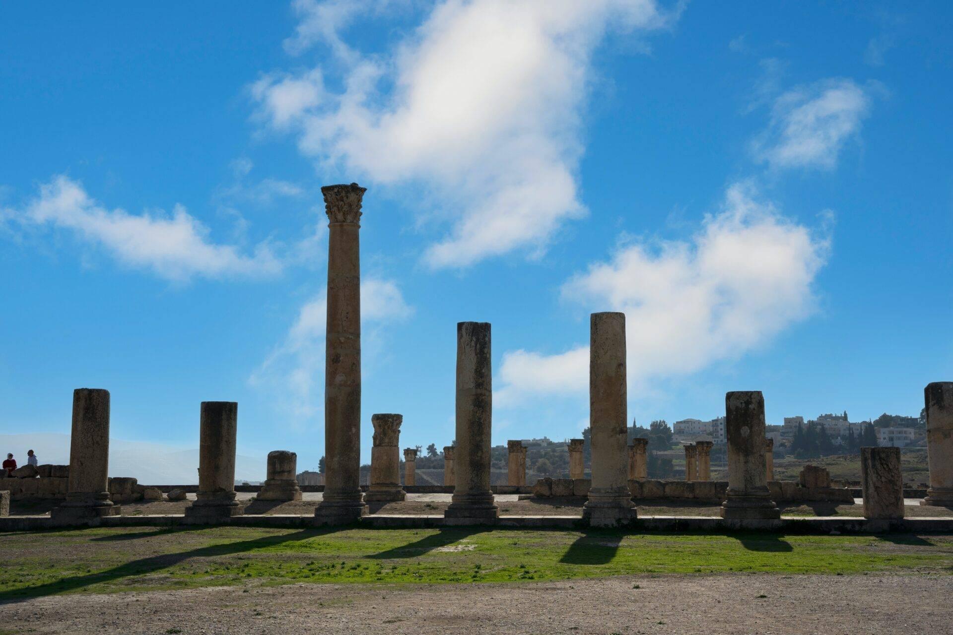Ruines antiques avec colonnes de pierre debout sur un terrain herbeux sous un ciel bleu nuageux