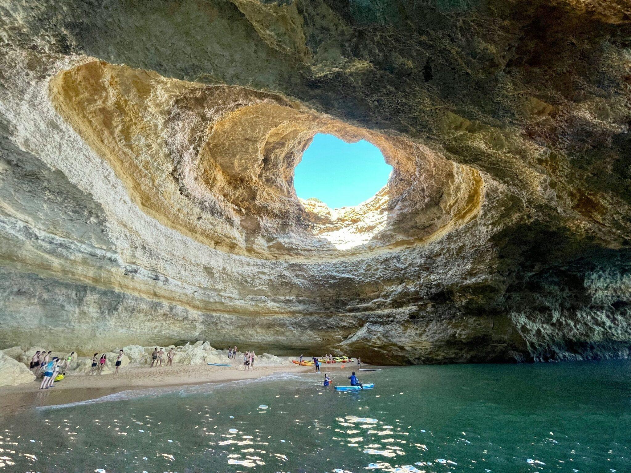 Une plage cachée sous une immense grotte calcaire avec un trou circulaire laissant entrer la lumière naturelle