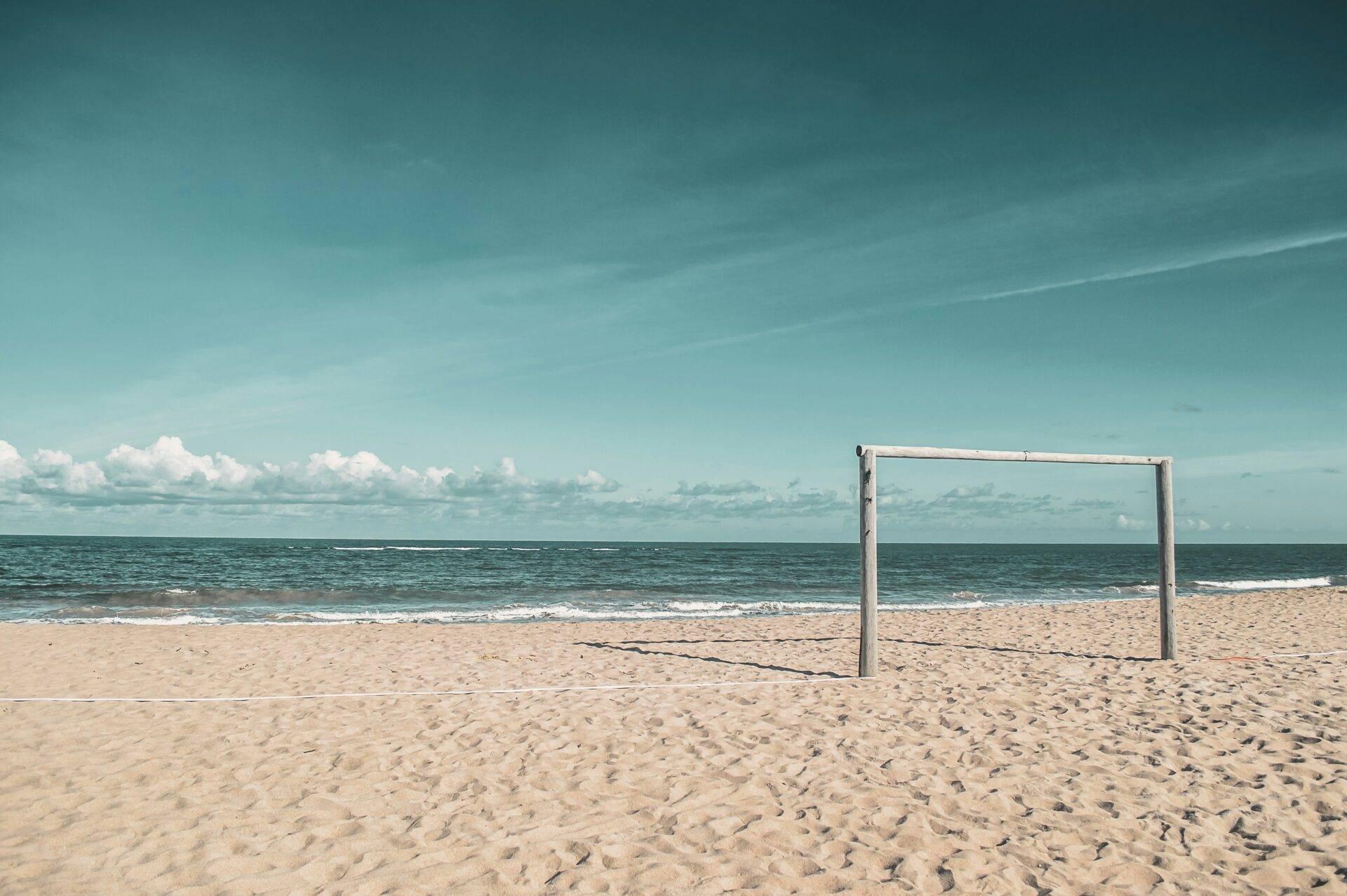 Un cadre de beach-volley vide sur une plage de sable fin face à l’océan turquoise sous un ciel dégagé