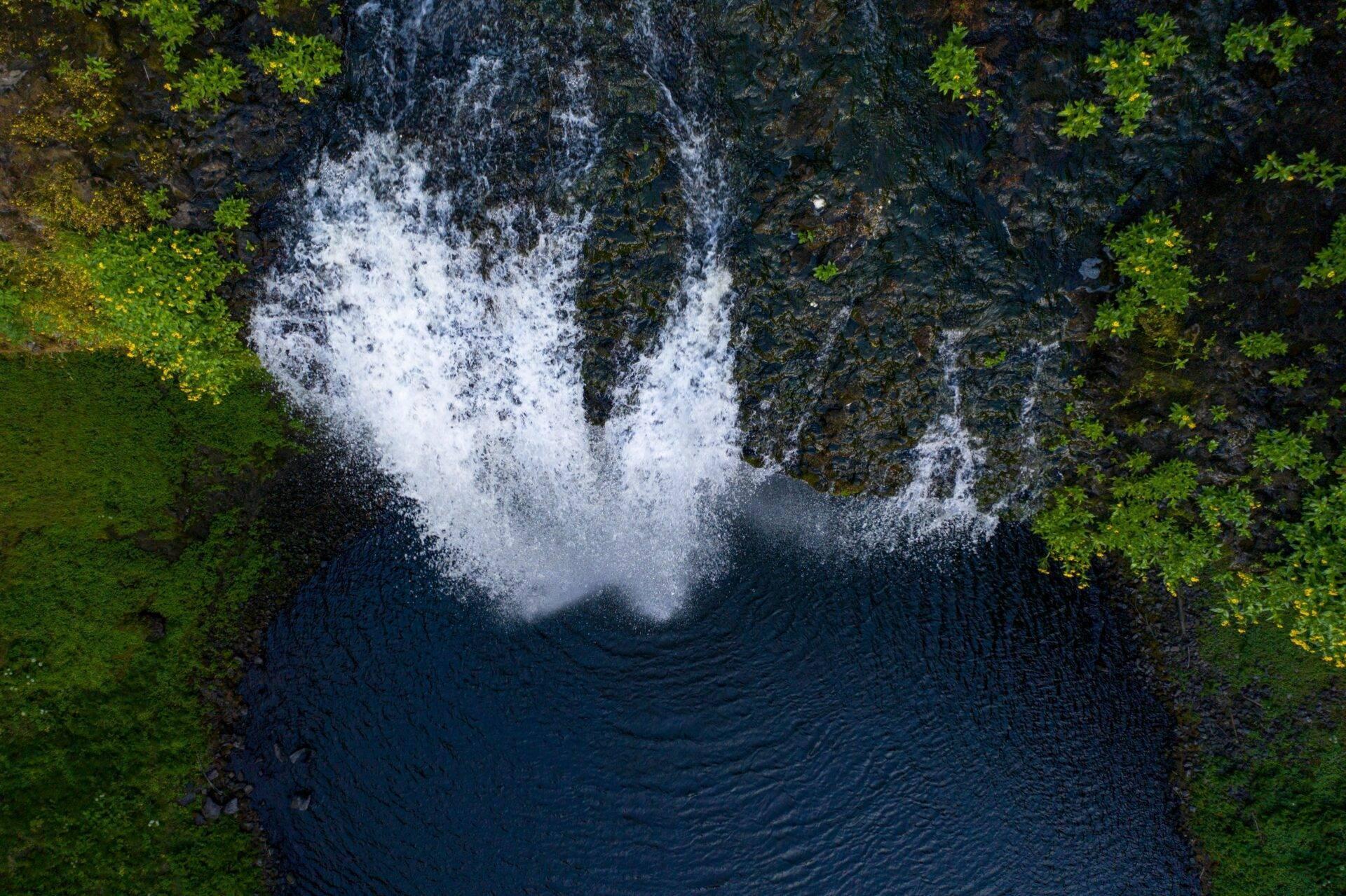 Vue aérienne d’une cascade tumultueuse s’écoulant dans un bassin rocheux entouré de végétation verte luxuriante