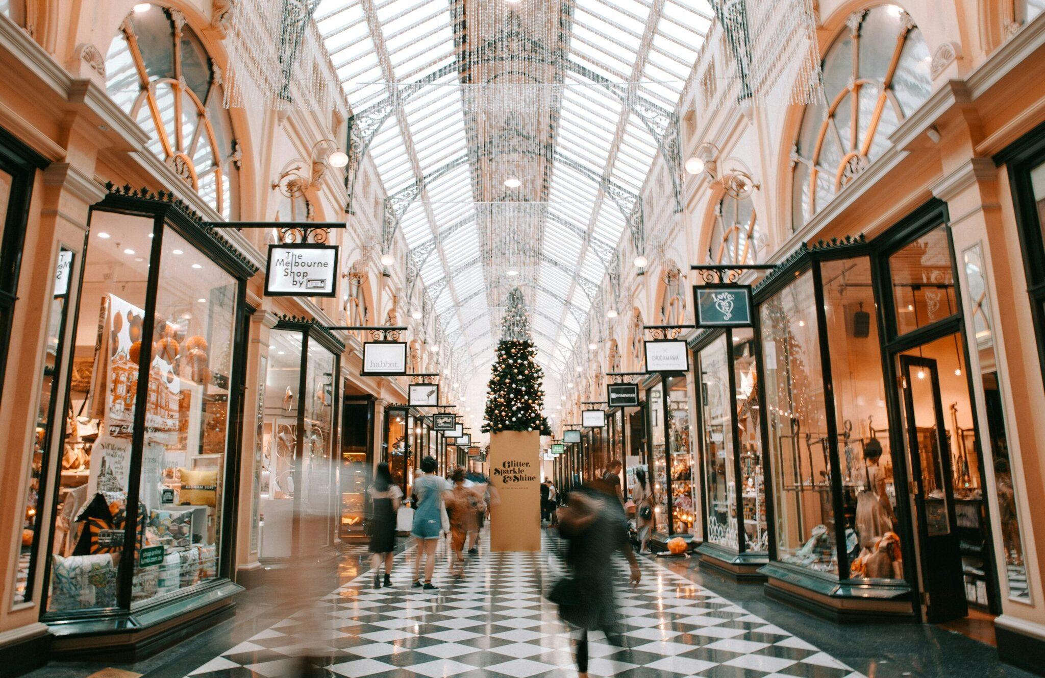Une galerie commerciale couverte au plafond vitrés, décorée d’un sapin de Noël, avec boutiques illuminées et quelques visiteurs