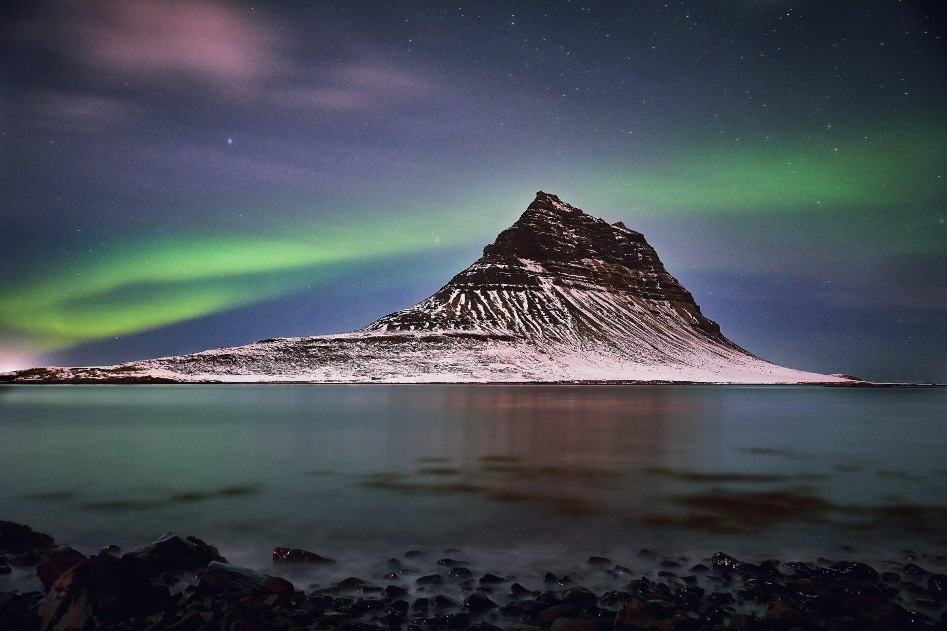 Une montagne enneigée se reflète dans une baie glaciale sous une aurore boréale verte et des étoiles