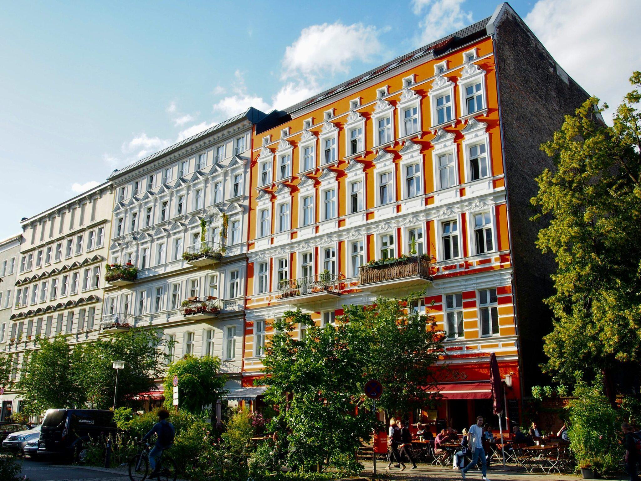 Immeuble coloré de style Gründerzeit avec façade orange et rouge, terrasse animée au rez-de-chaussée, lierre sur les côtés