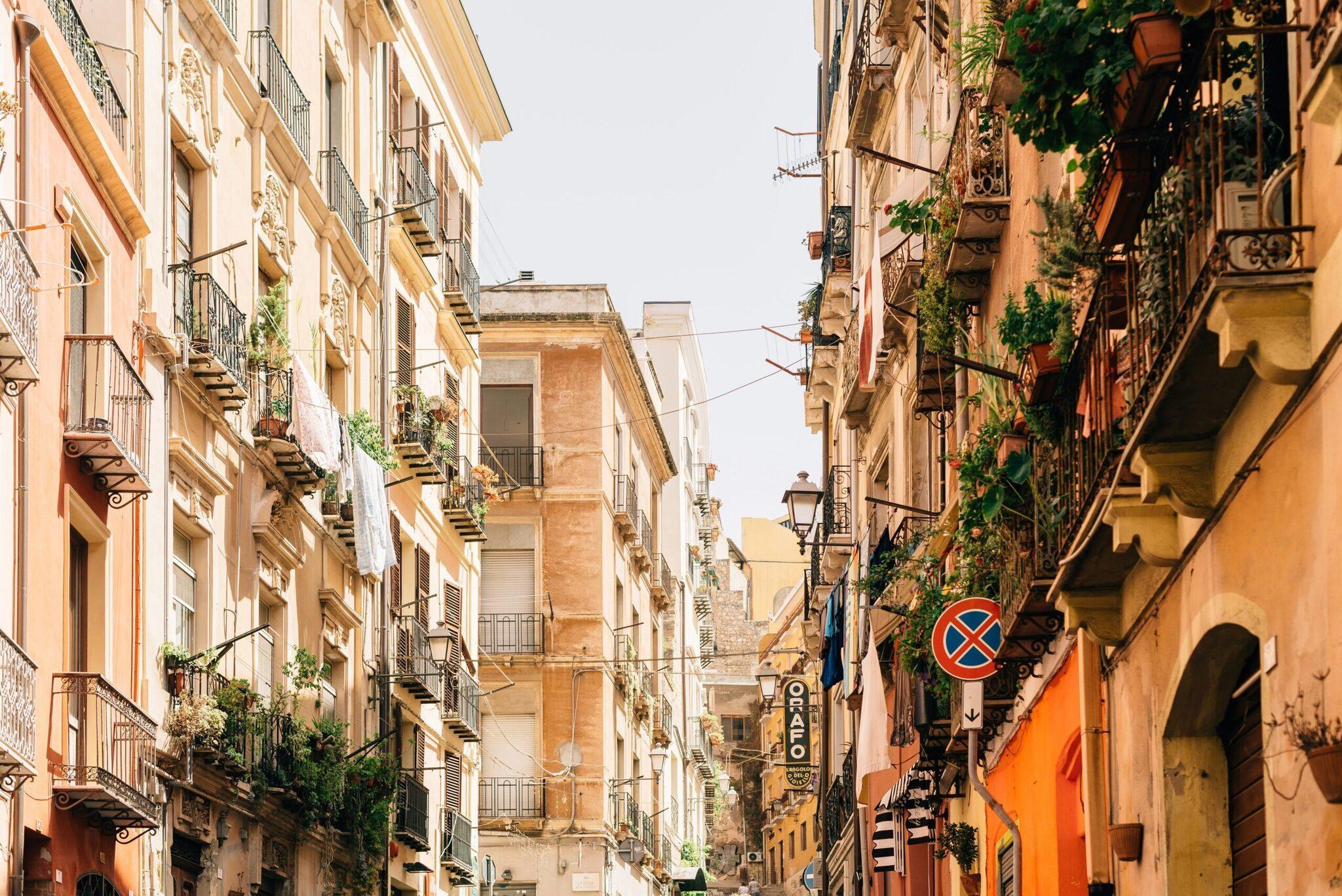 A narrow Mediterranean alleyway with colourful facades, ornate balconies, climbing plants and street signs