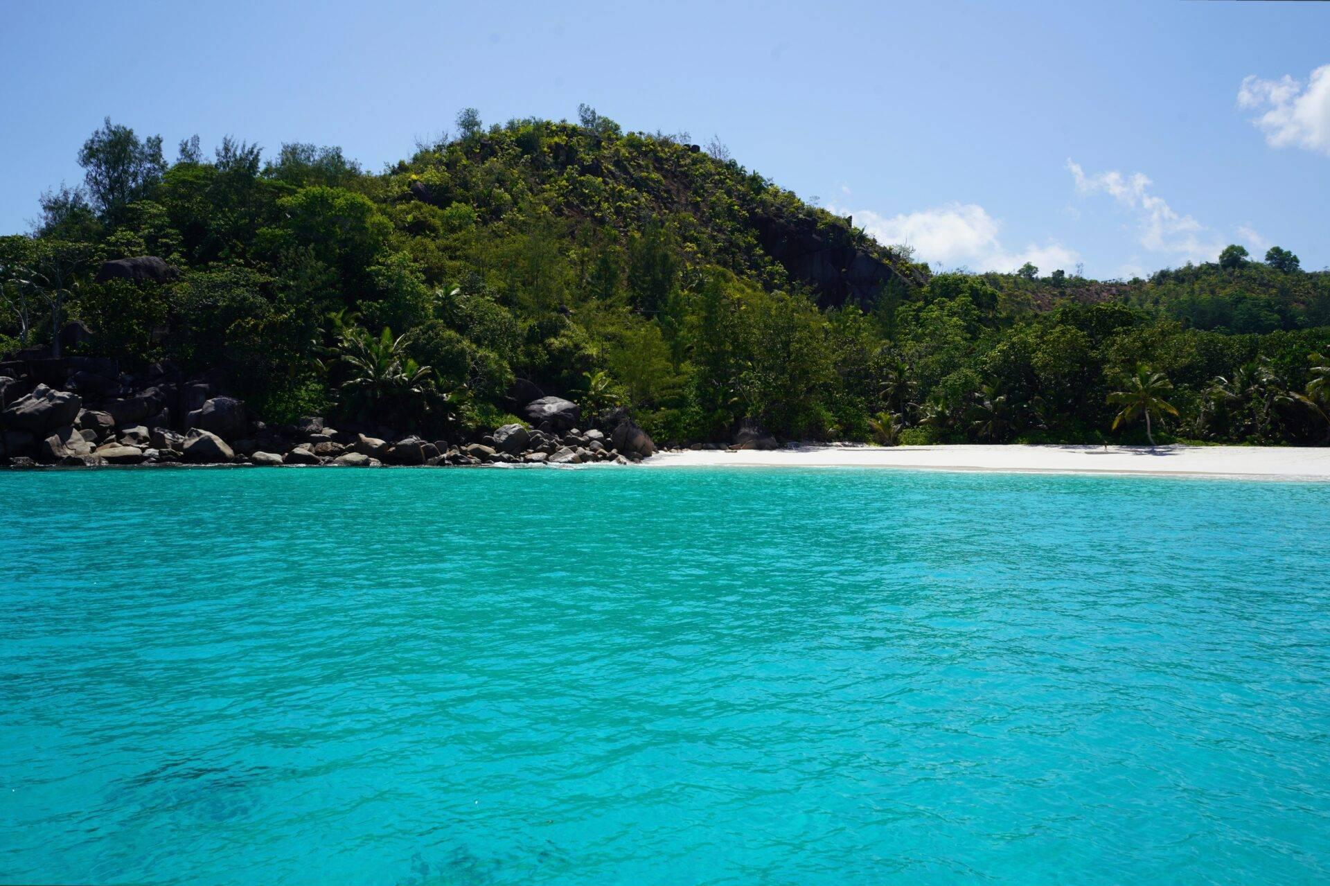 Une plage de sable blanc et turquoise bordée de rochers et de végétation tropicale luxuriante sous un ciel bleu