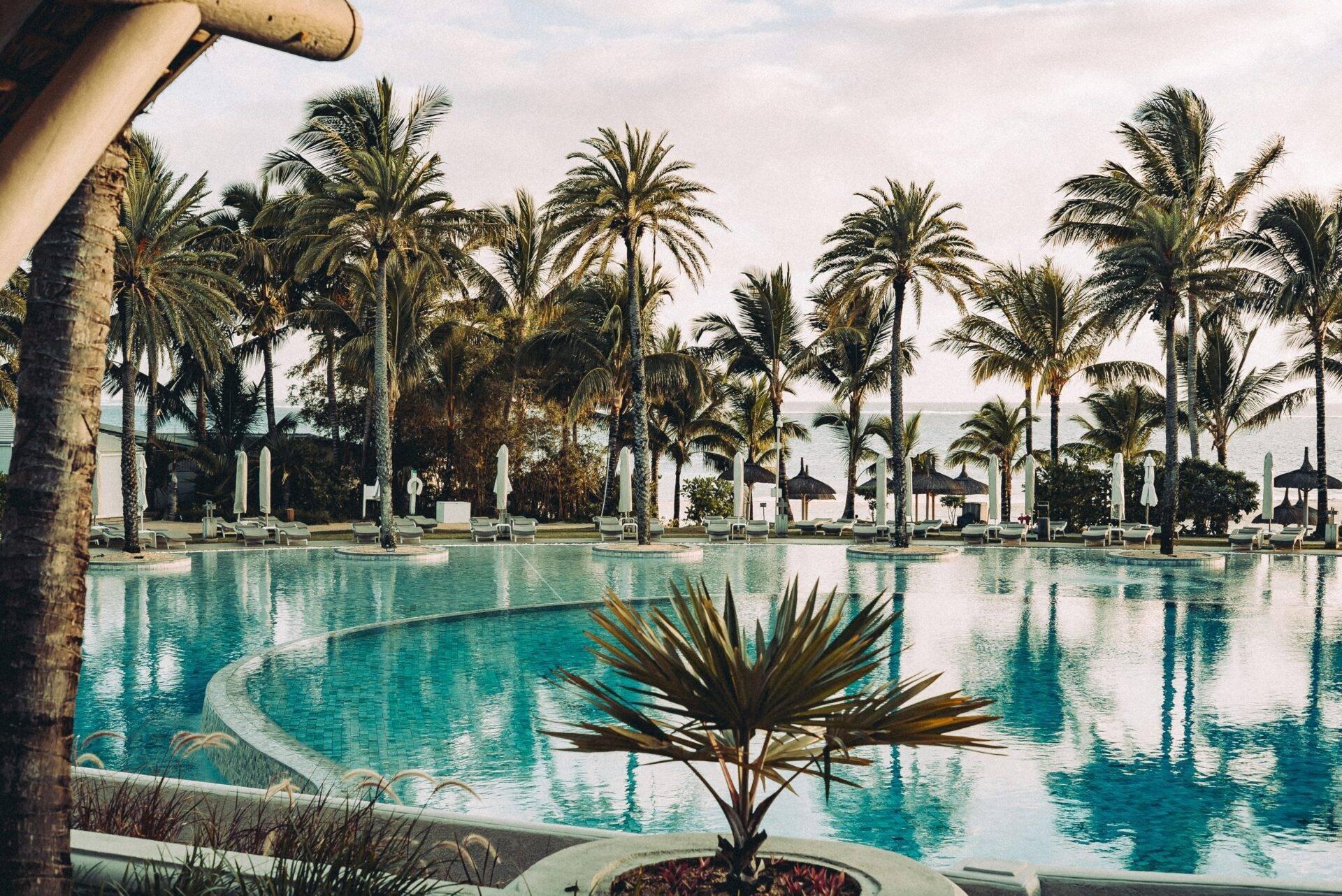 Une grande piscine turquoise bordée de palmiers et de transats blancs dans un resort luxueux tropical