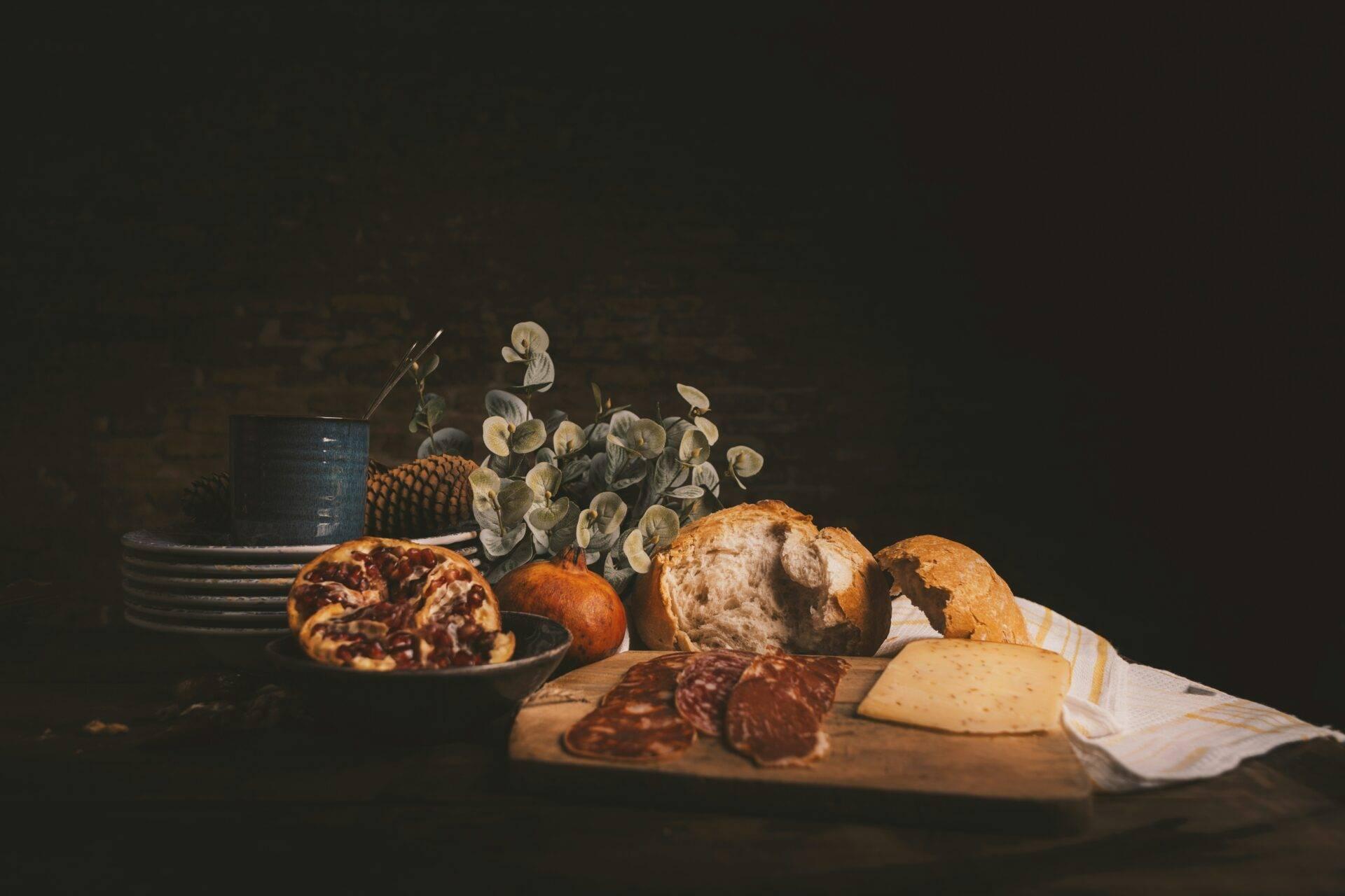 Composition culinaire avec pain, charcuterie, fromage, fruits et fleurs séchées sur fond sombre