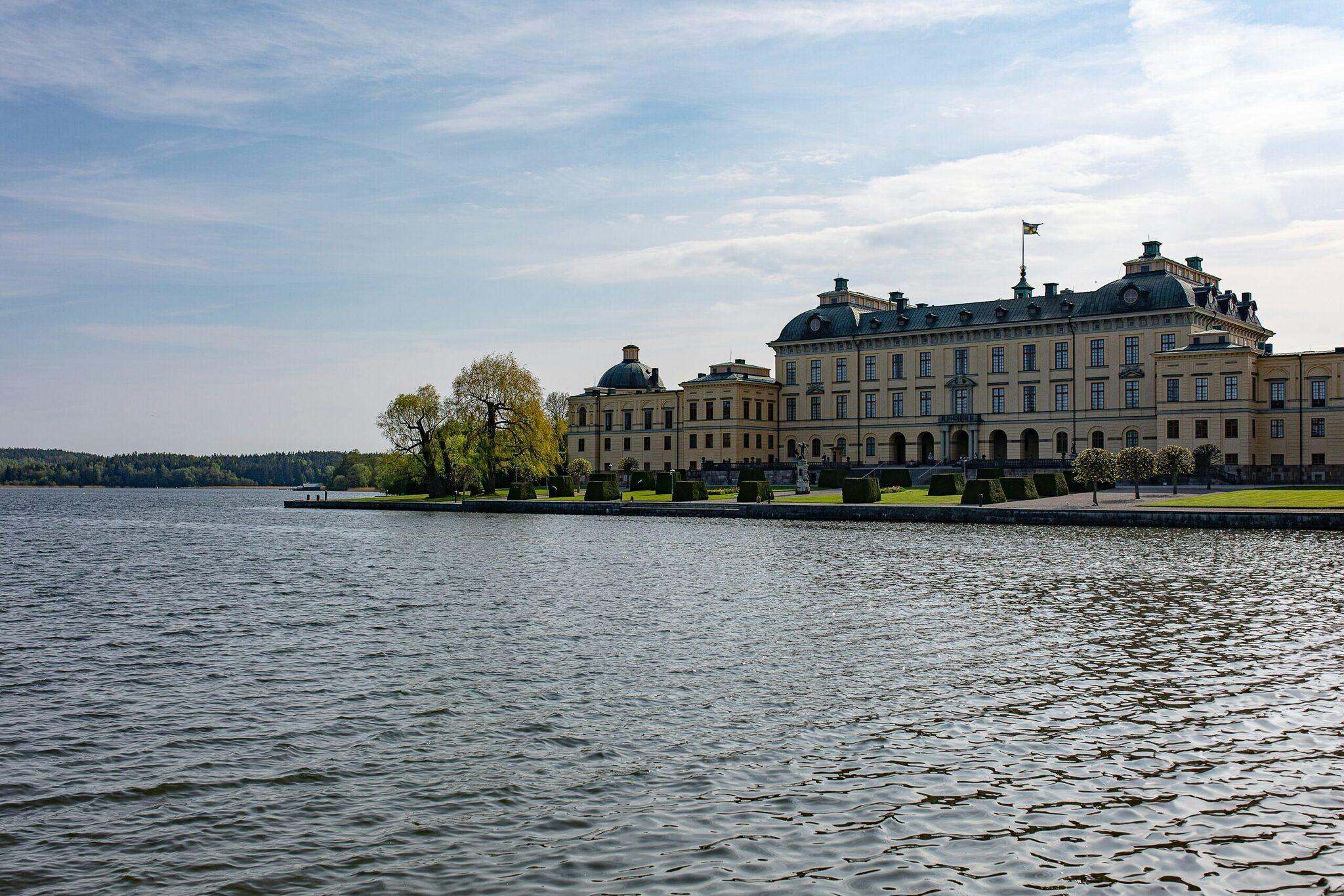 Un élégant palais de style rococo aux façades jaunes situé sur une île lacustre, entouré de verdure et photographié depuis l’eau par temps clair