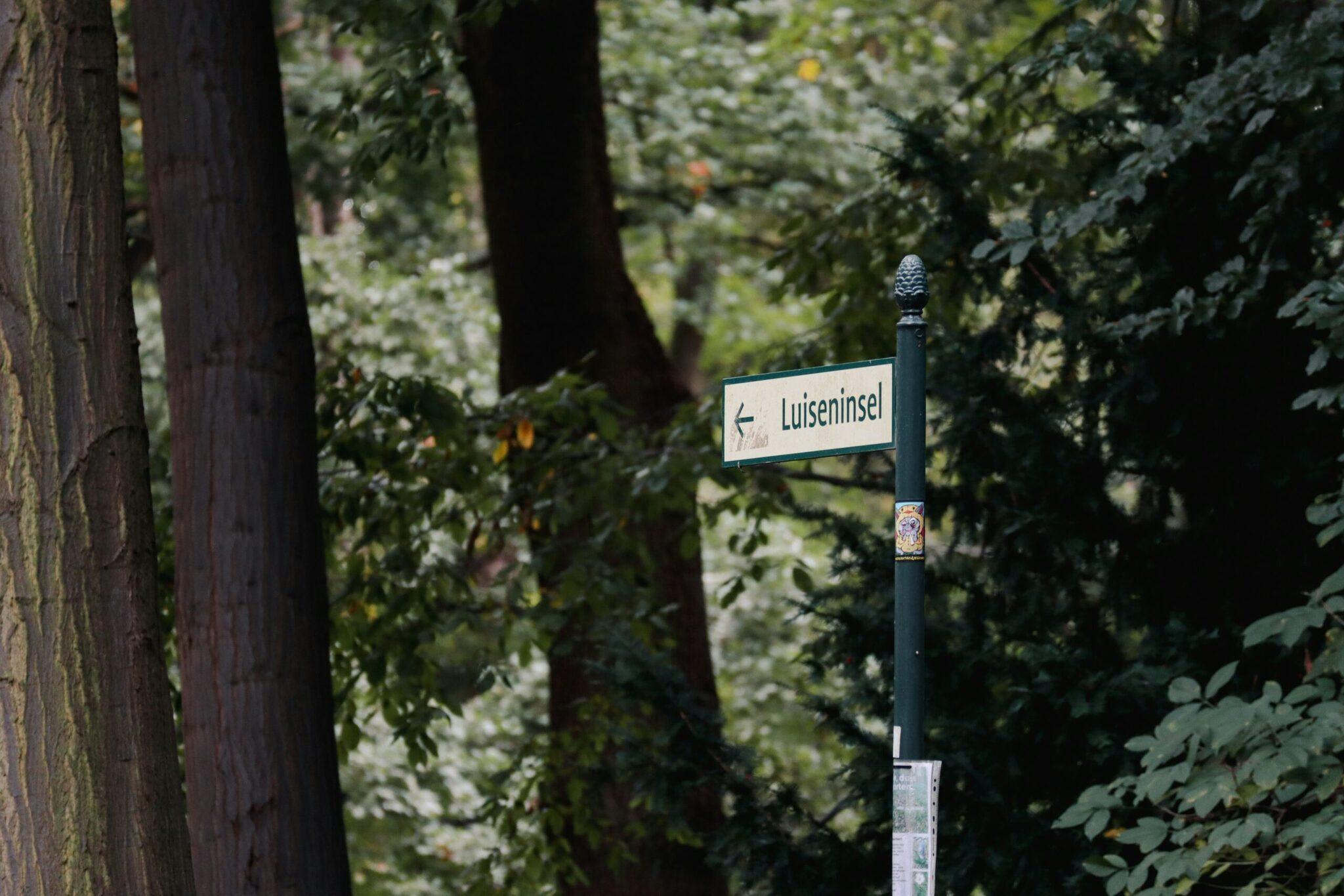 Plaque de rue « Luiseninsel » dans une ruelle verdoyante bordée de vieux murs de briques et d’arbres