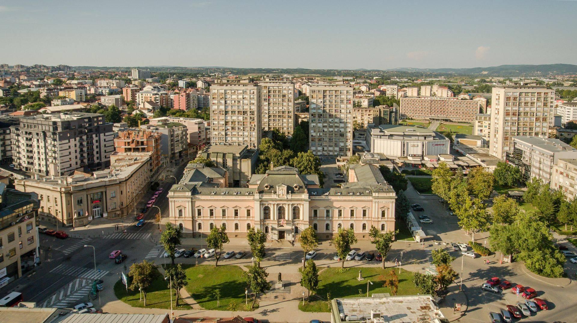 Vue aérienne d’une ville avec un bâtiment classique blanc au centre, entouré de modernismes résidentiels et d’espaces verts