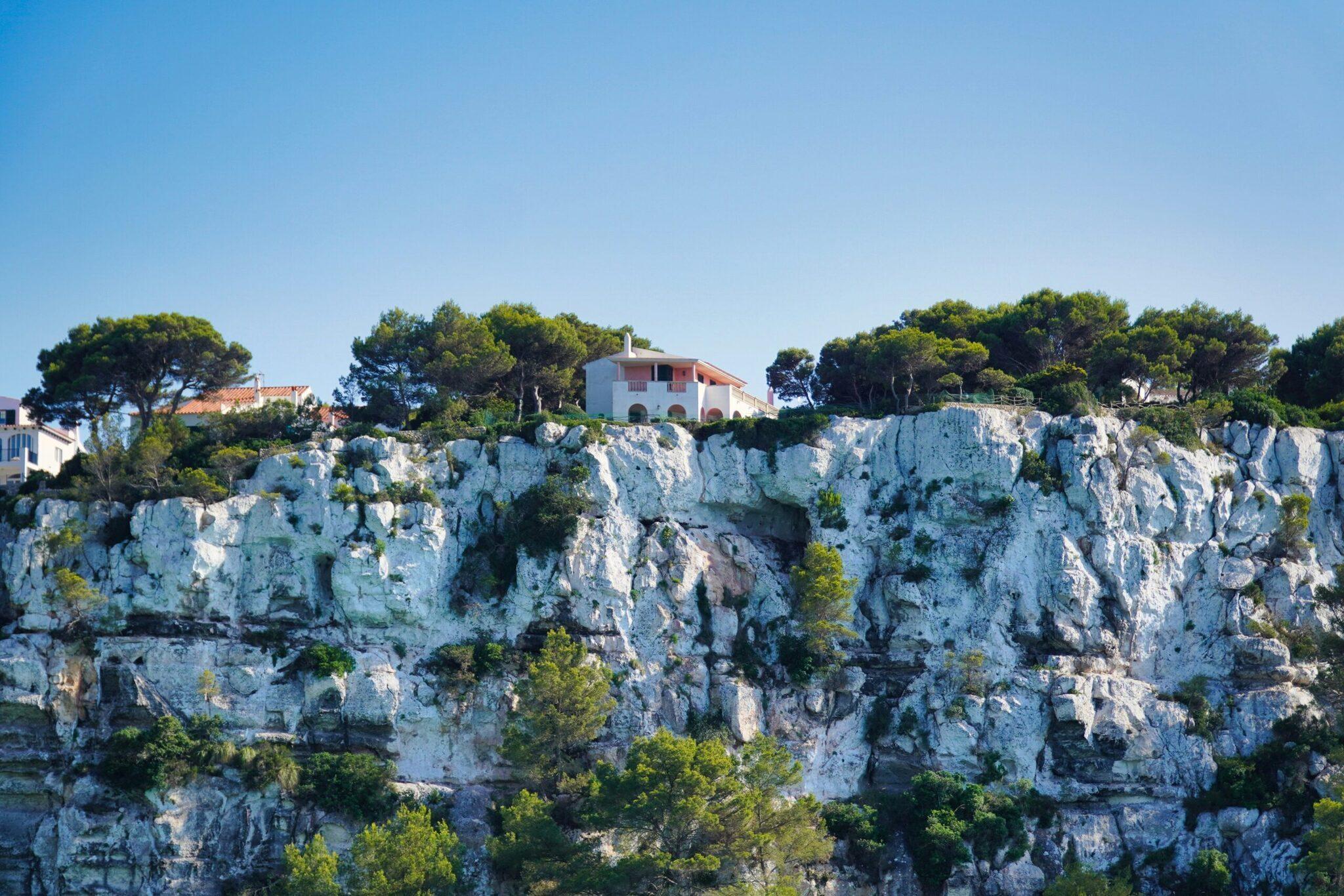 Maison méditerranéenne blanche perchée sur une falaise calcaire escarpée entourée de végétation