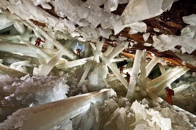 Des explorateurs marchent entre d’immenses cristaux de sélénite translucide dans une grotte souterraine spectaculaire