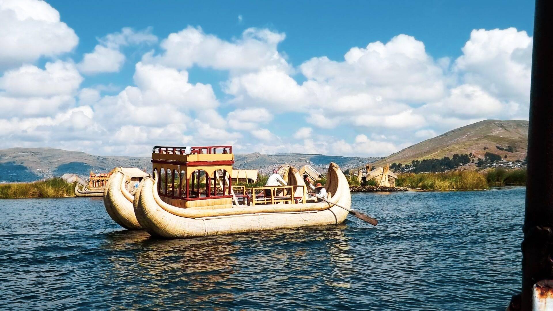 Un bateau traditionnel en roseaux avec cabine rouge navigue sur un lac d’altitude entouré de montagnes arides
