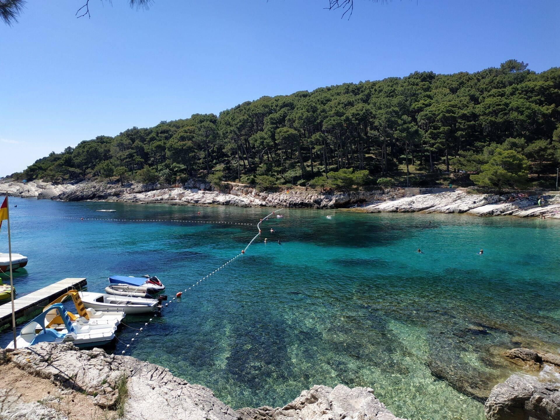 Une crique méditerranéenne aux eaux turquoise avec bateaux amarrés, falaises rocheuses et forêt de pins