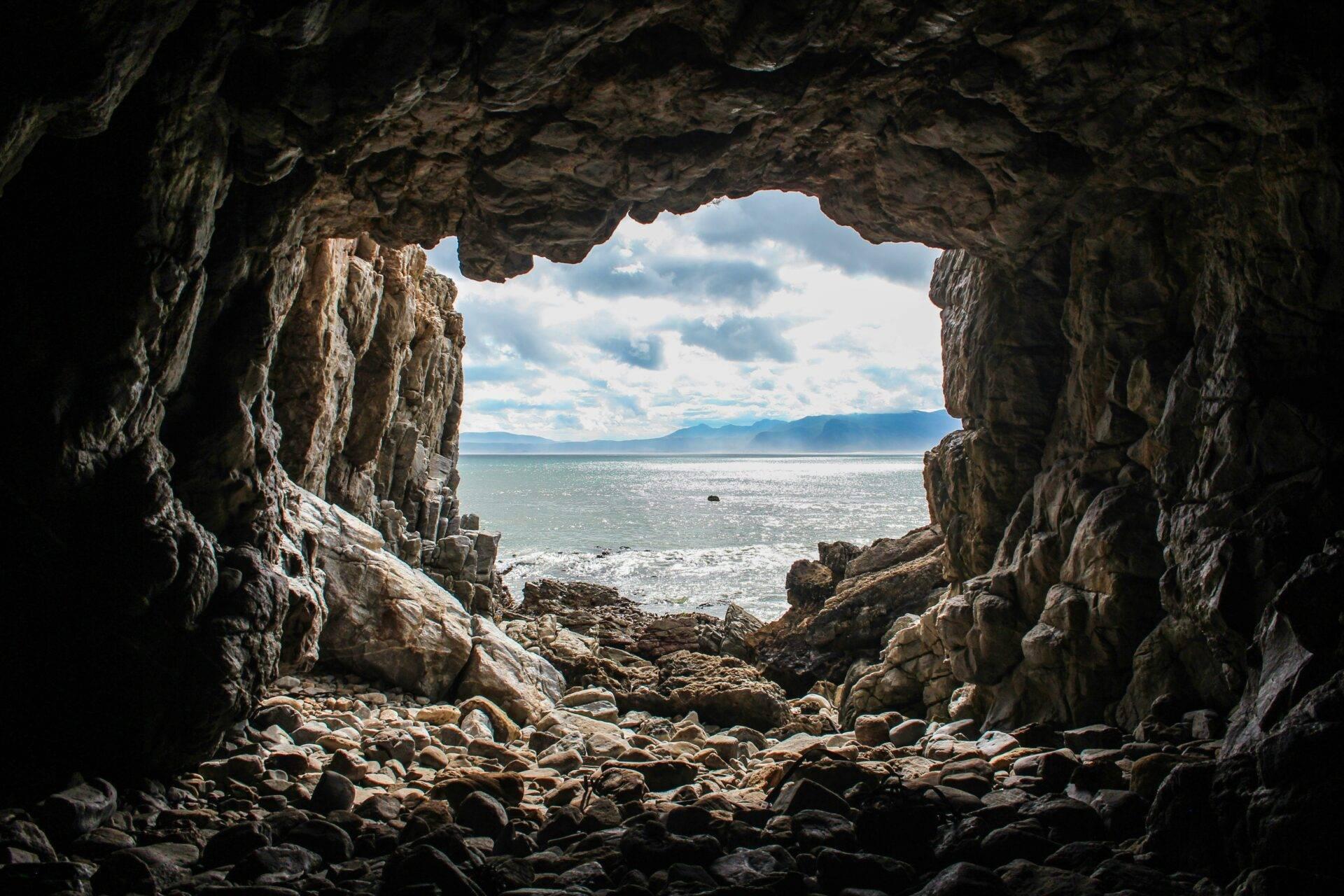 Vue depuis l’intérieur d’une grotte côtière sur la mer, des montagnes et un ciel nuageux