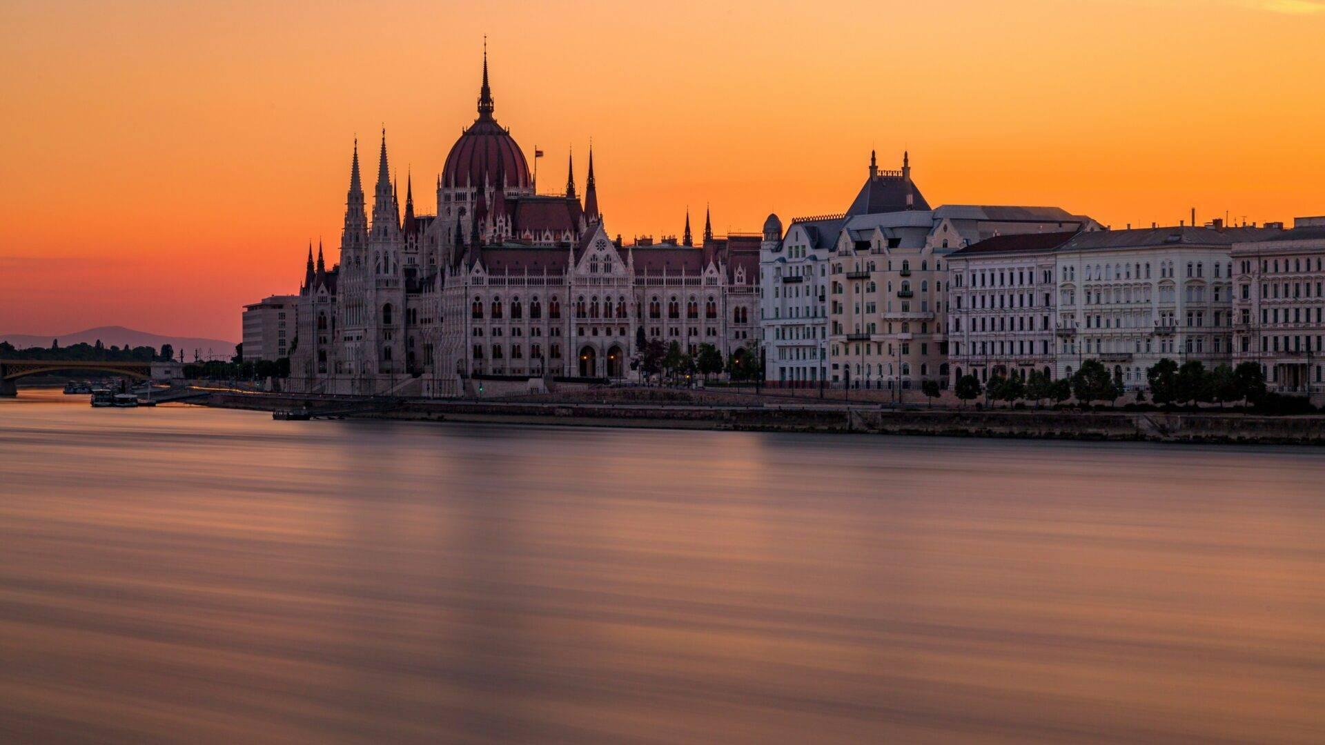 Édifice gothique imposant avec dôme central et spires pointues au bord d’un fleuve au coucher de soleil