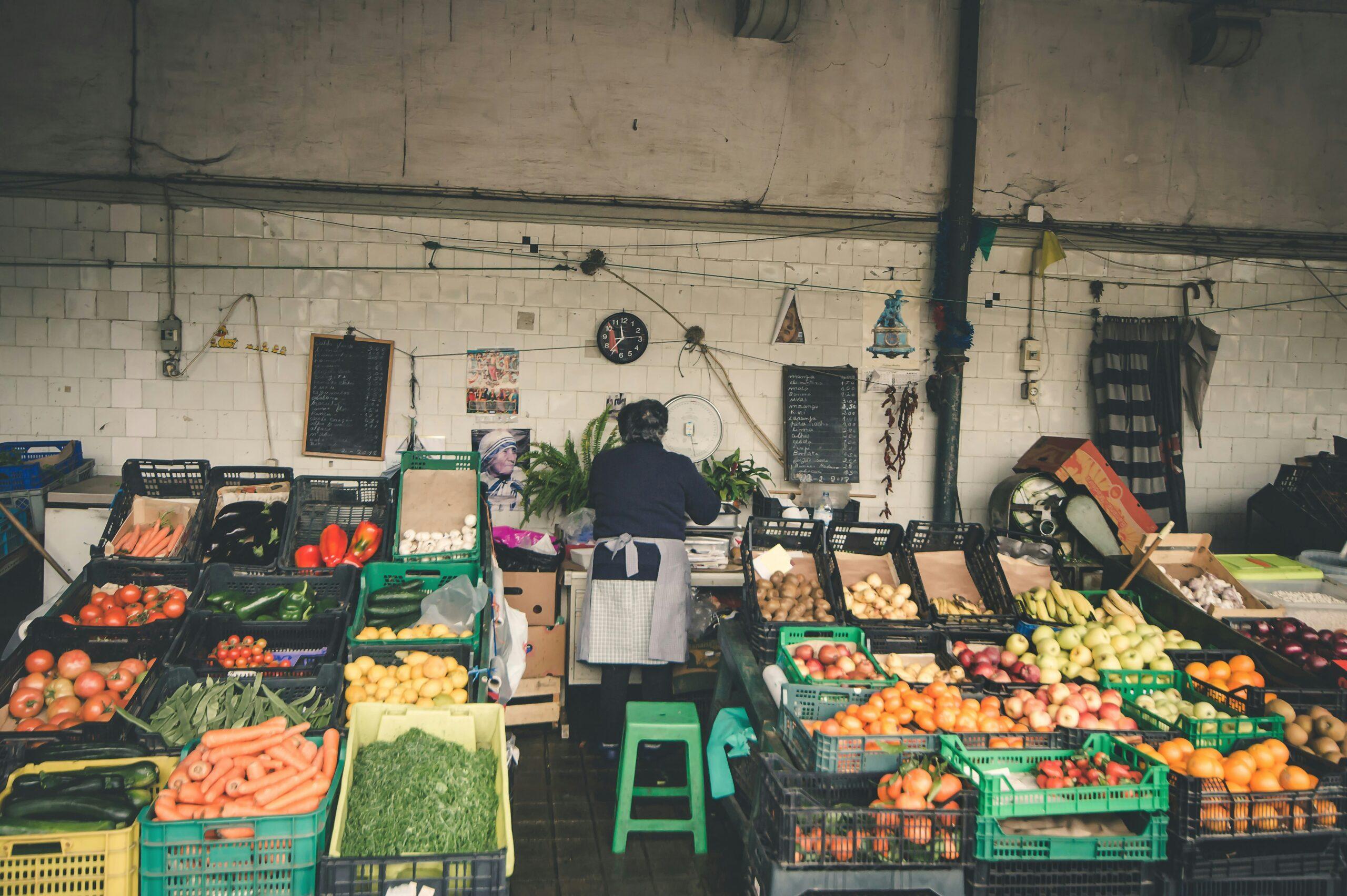 Un vendeur de fruits et légumes frais dans un marché couvert traditionnel avec étalages colorés et murs de carrelage blanc