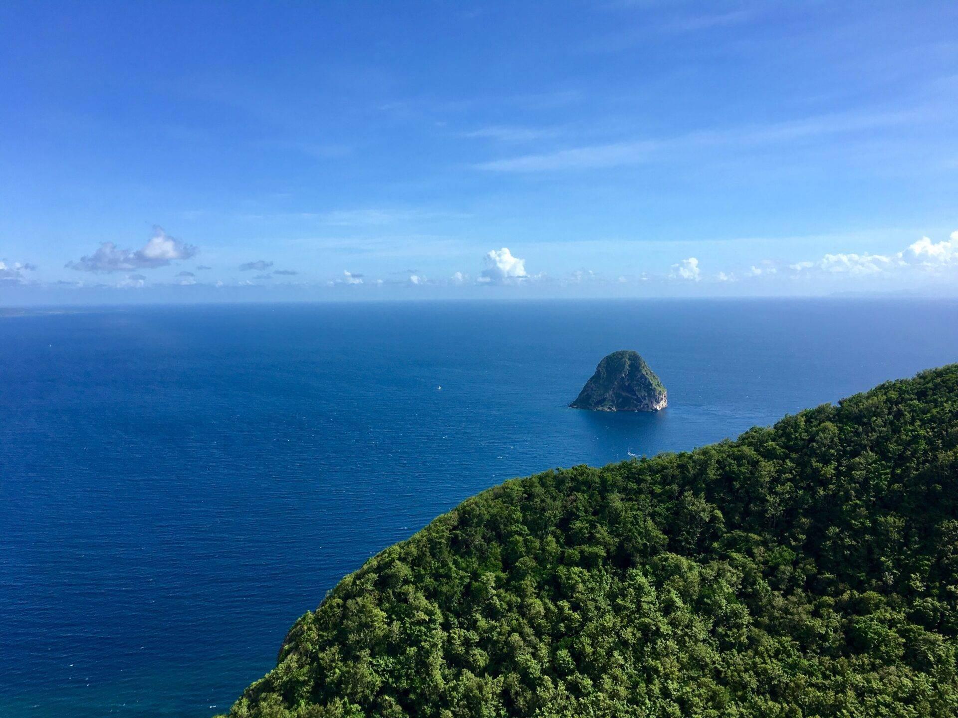 Vue aérienne d’une côte verdoyante dominant une mer turquoise avec un îlot rocheux isolé au large