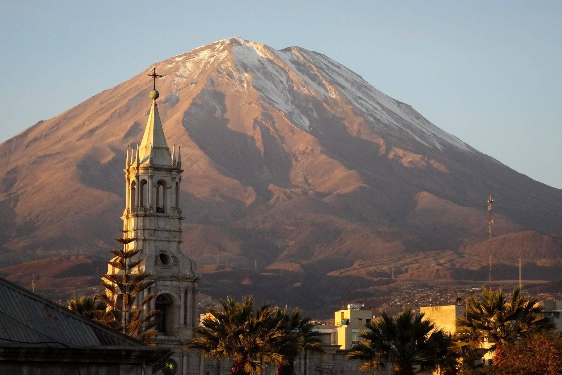 Un clocher blanc avec croix dorée face à un volcan enneigé dans les Andes péruviennes