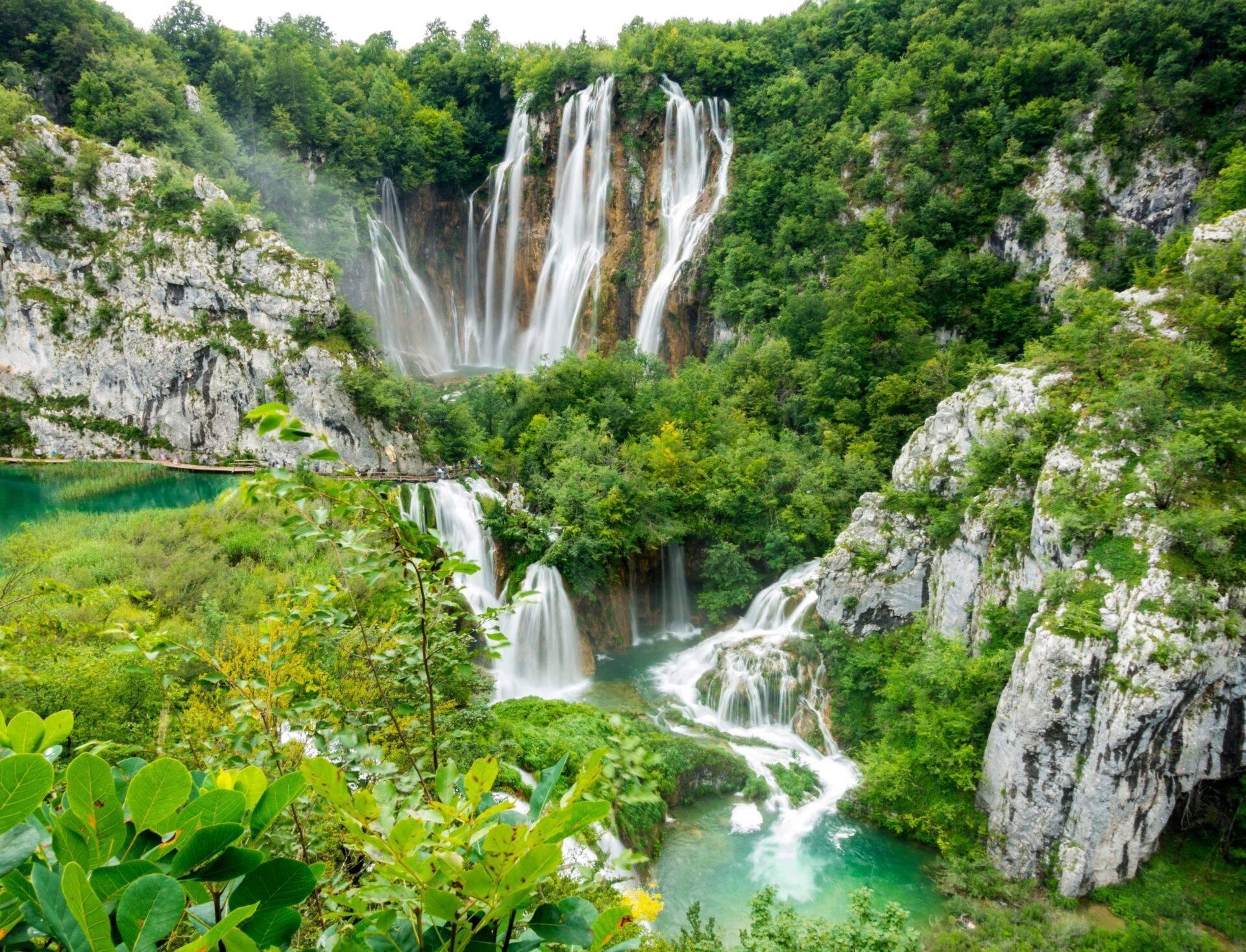 Cascades spectaculaires dévalant des falaises calcaires dans une gorge boisée avec lacs turquoise