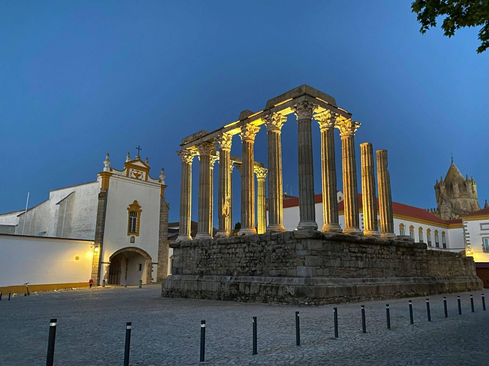 Ruines romaines illuminées avec colonnes corinthiennes et églises blanches en arrière-plan au crépuscule