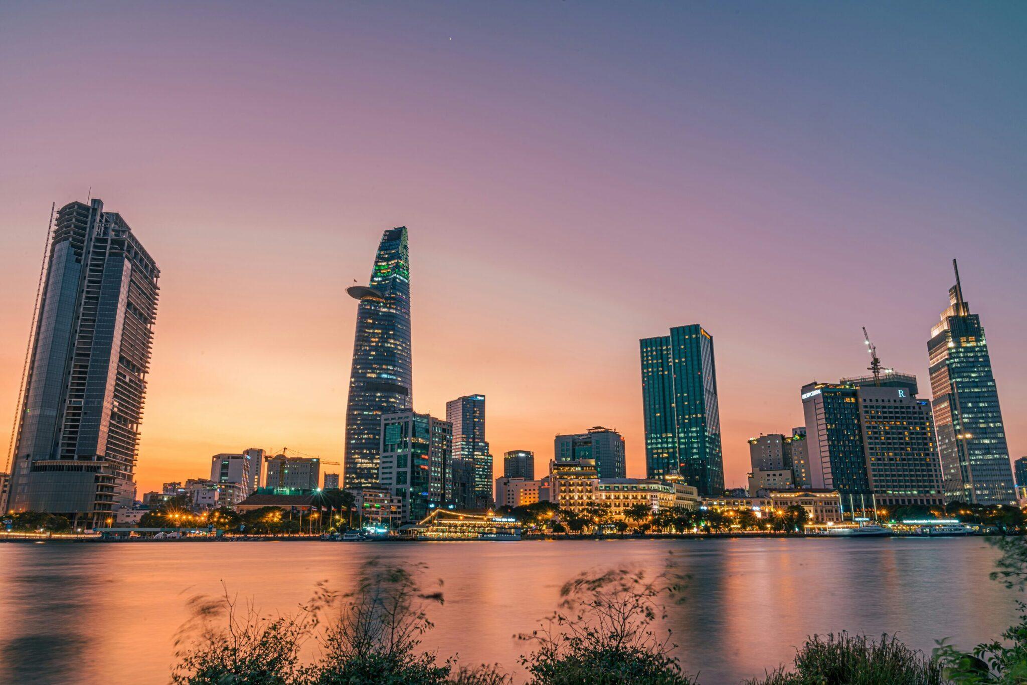 Skyline urbain illuminé au coucher du soleil avec gratte-ciel modernes se reflétant dans l’eau d’un fleuve