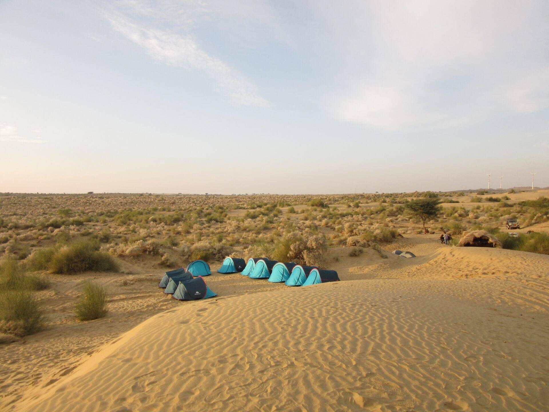 Campement de tentes bleues dans le désert du Rajasthan avec dunes de sable et végétation clairsemée