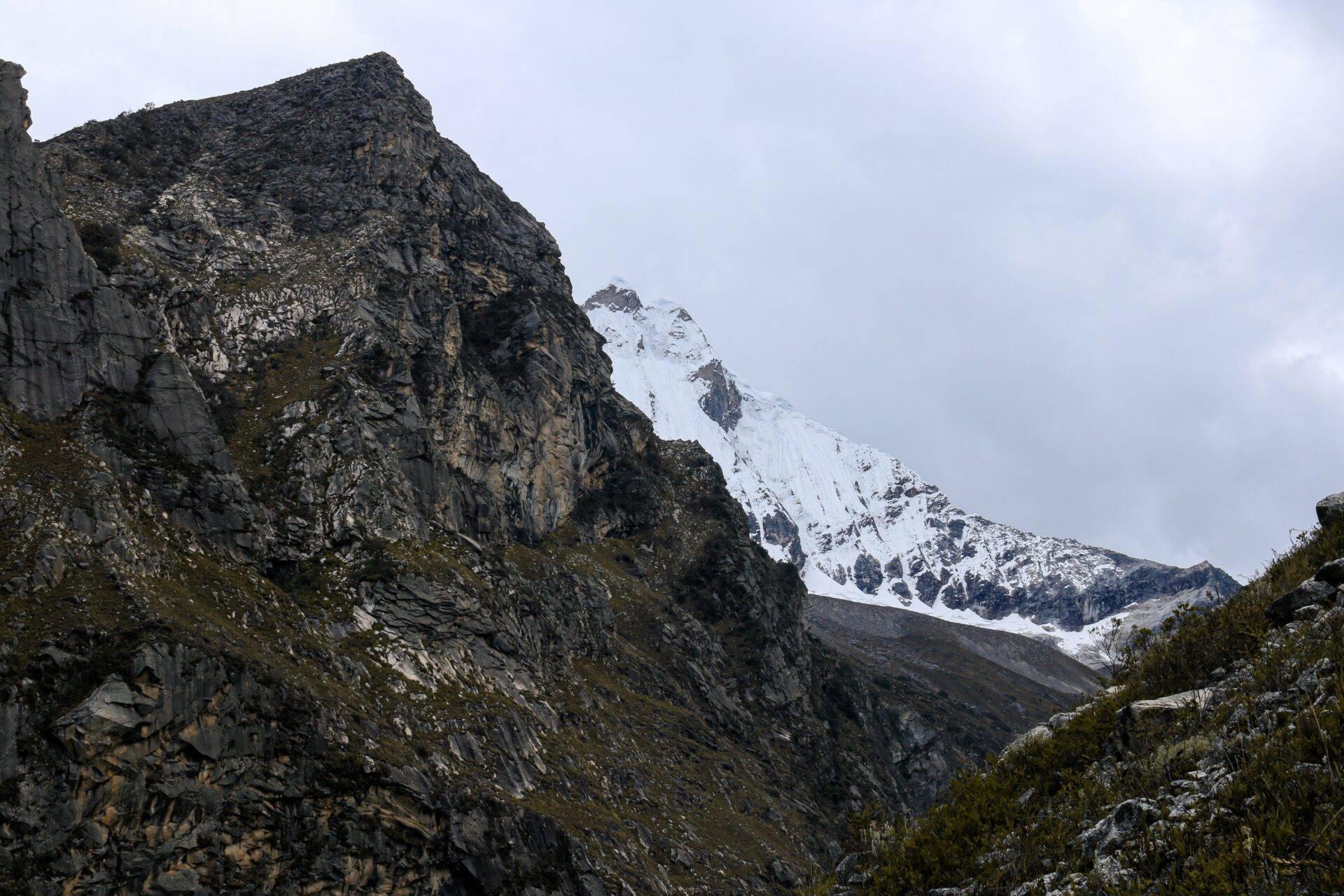 Vue d’une vallée alpine avec pics rocheux escarpés et montagne enneigée en arrière-plan sous ciel nuageux
