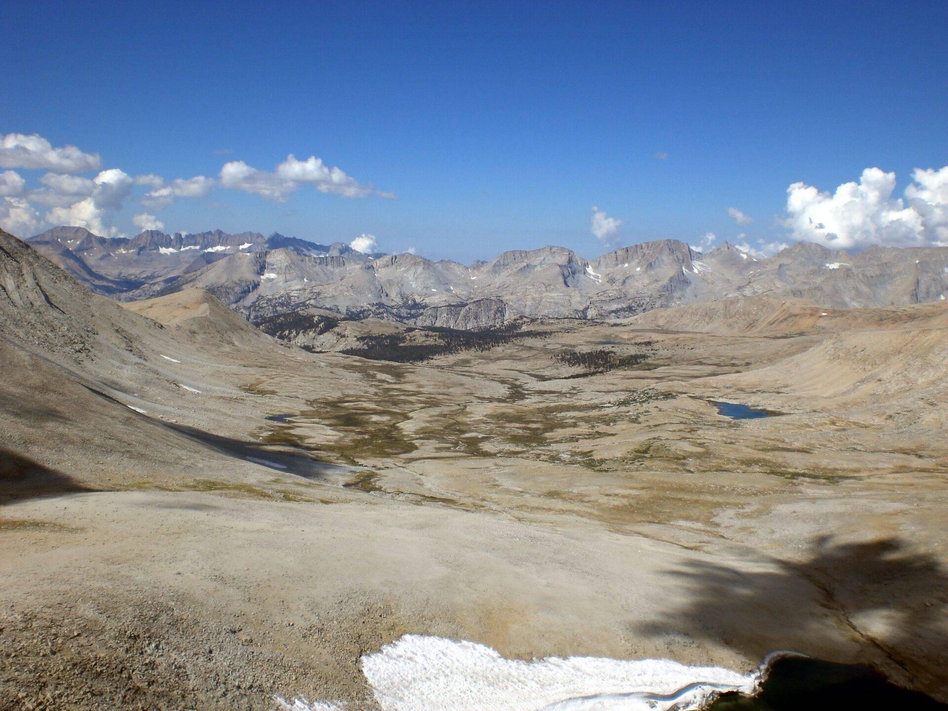 Vue panoramique d’une vallée alpine désertique avec lacs glaciaires, pics rocheux et neige résiduelle