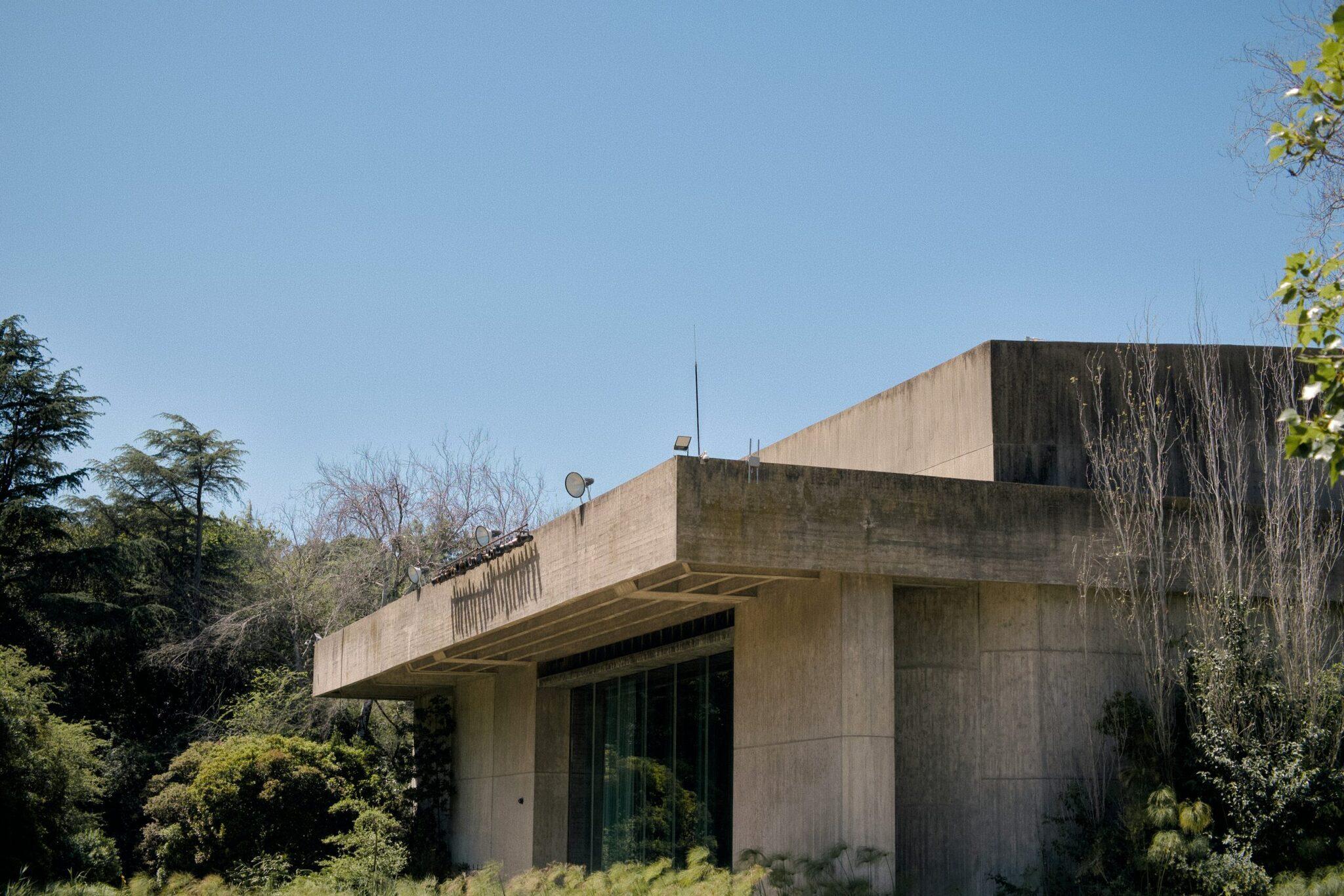 Bâtiment moderne en béton brut avec terrasse surplombante, entouré de végétation luxuriante sous ciel dégagé
