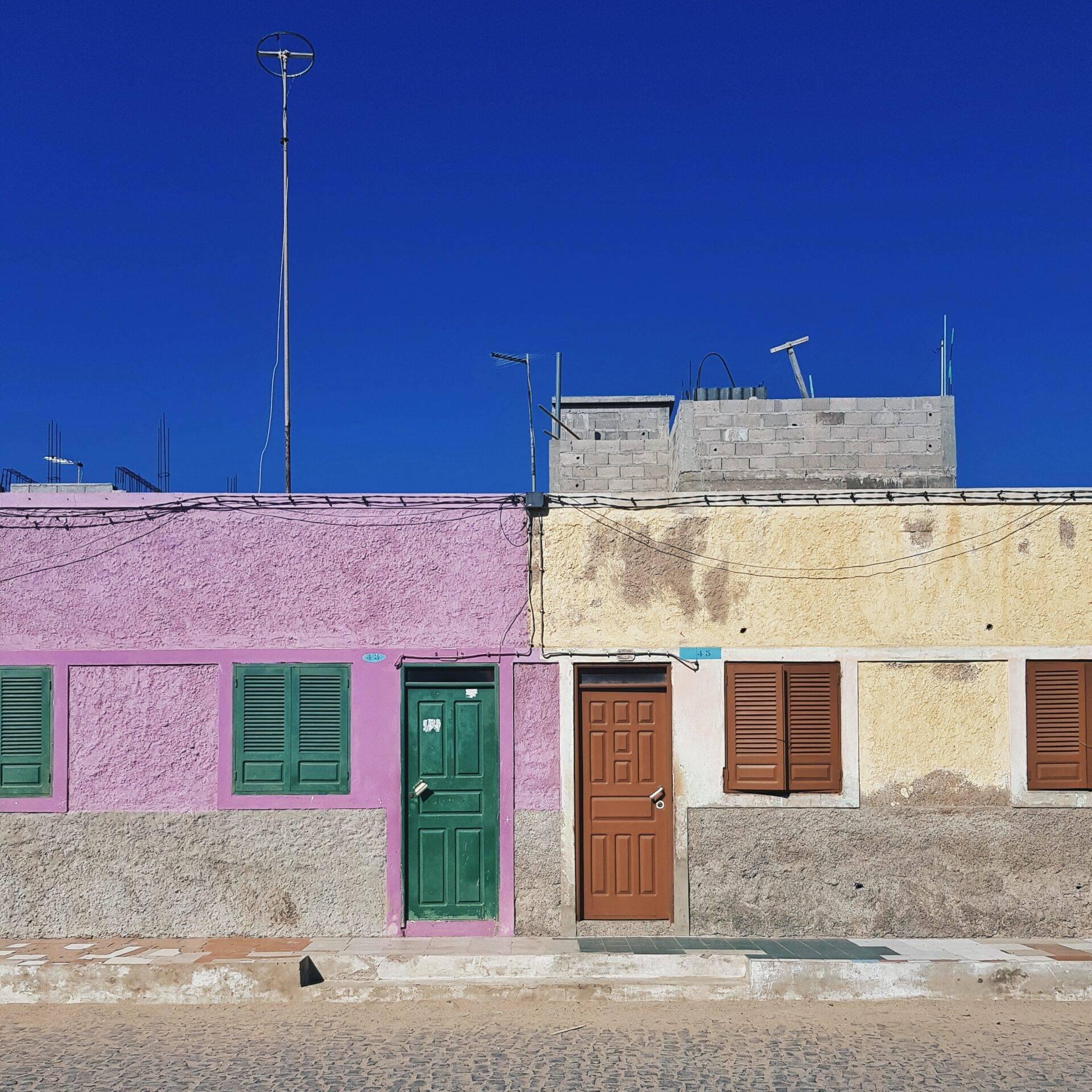 Façade colorée de maisons roses et beiges avec portes vertes et marron sous un ciel bleu intense