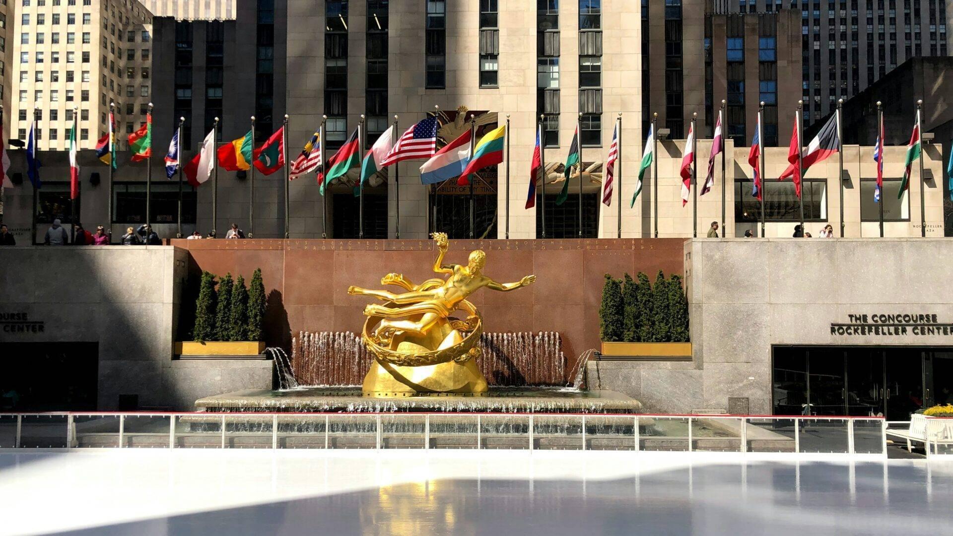 Place publique emblématique avec statue dorée, drapeaux internationaux et patinoire glacée en hiver à New York