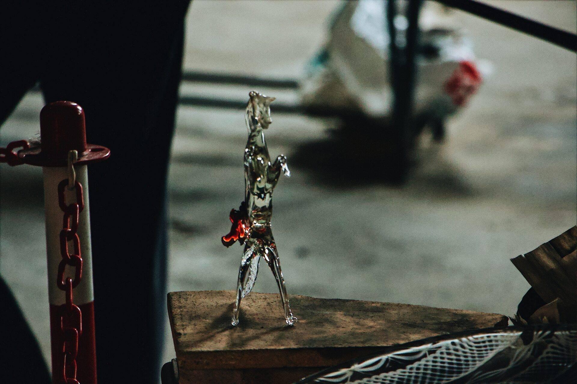 Une figurine en verre posée sur du bois ancien, avec une chaîne rouge et des objets flous en arrière-plan