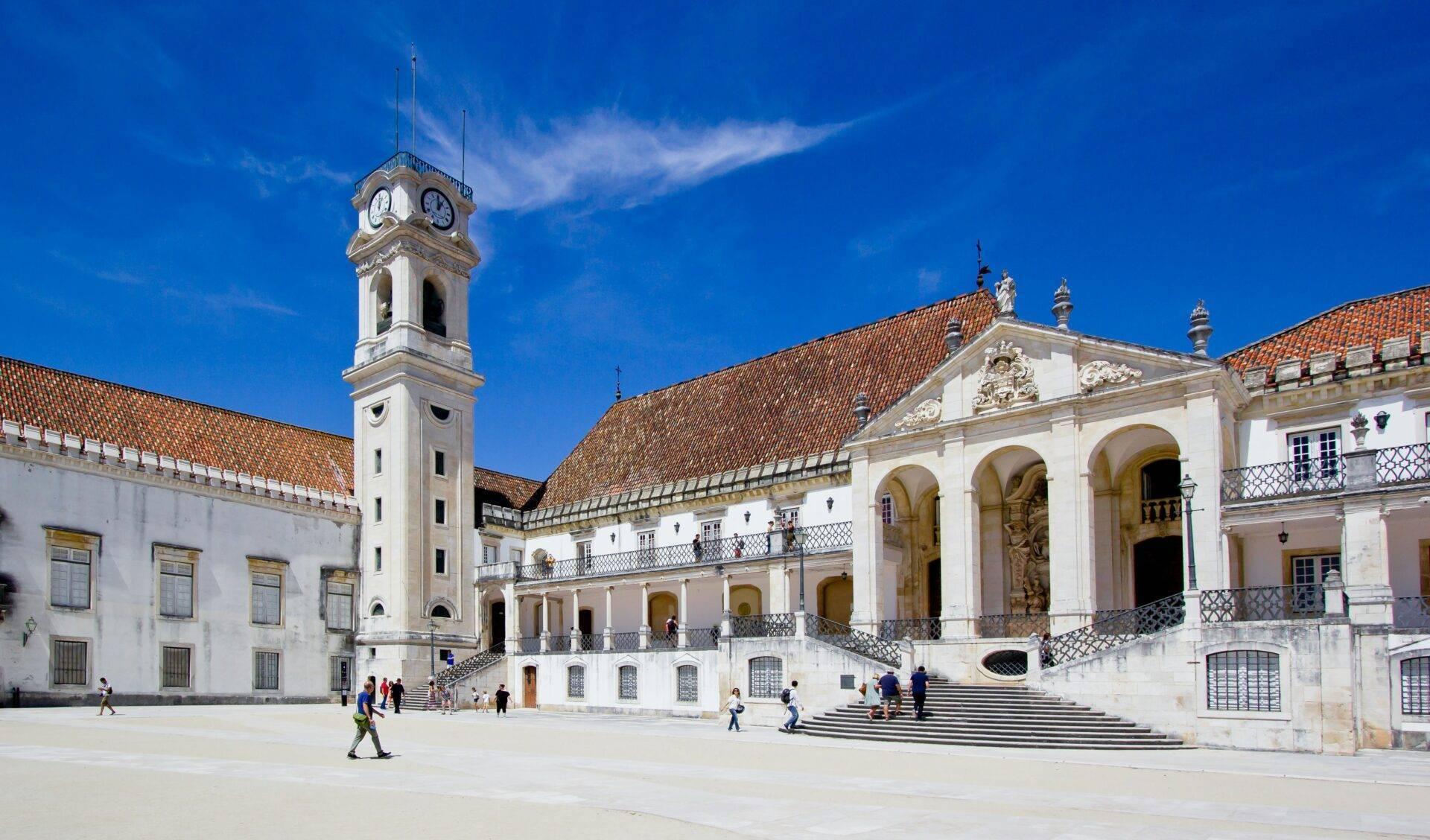 Cour intérieure d’une université historique avec clocher blanc, bâtiments coloniaux et carrelage azulejos sous ciel bleu