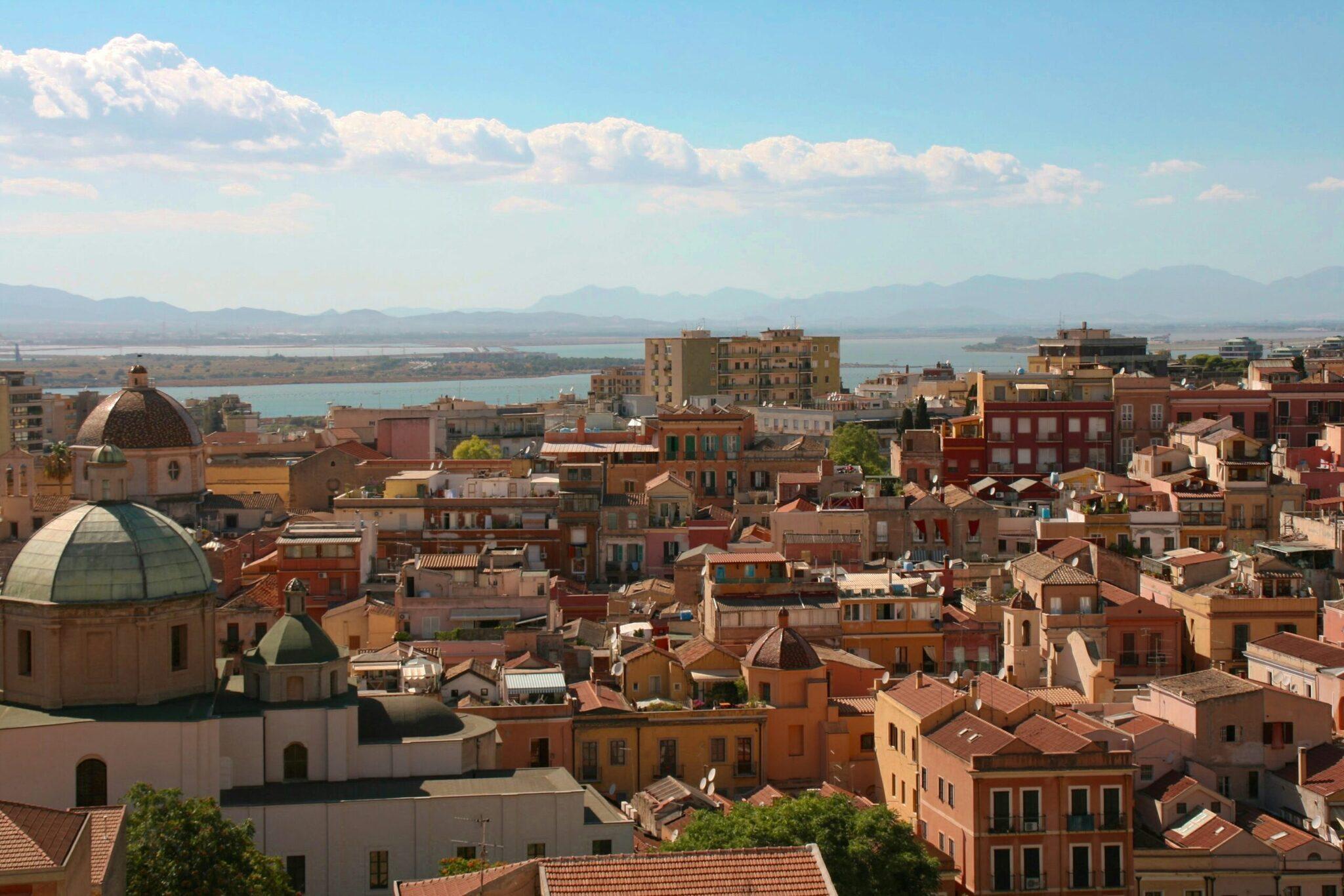 Panoramic view of a Mediterranean coastal city with a domed church, colourful architecture and turquoise sea in the background