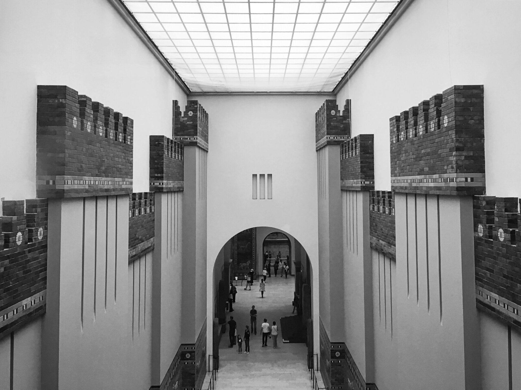 Reconstitution architecturale d’une porte de ville antique avec tours massives et visiteurs traversant une arche centrale