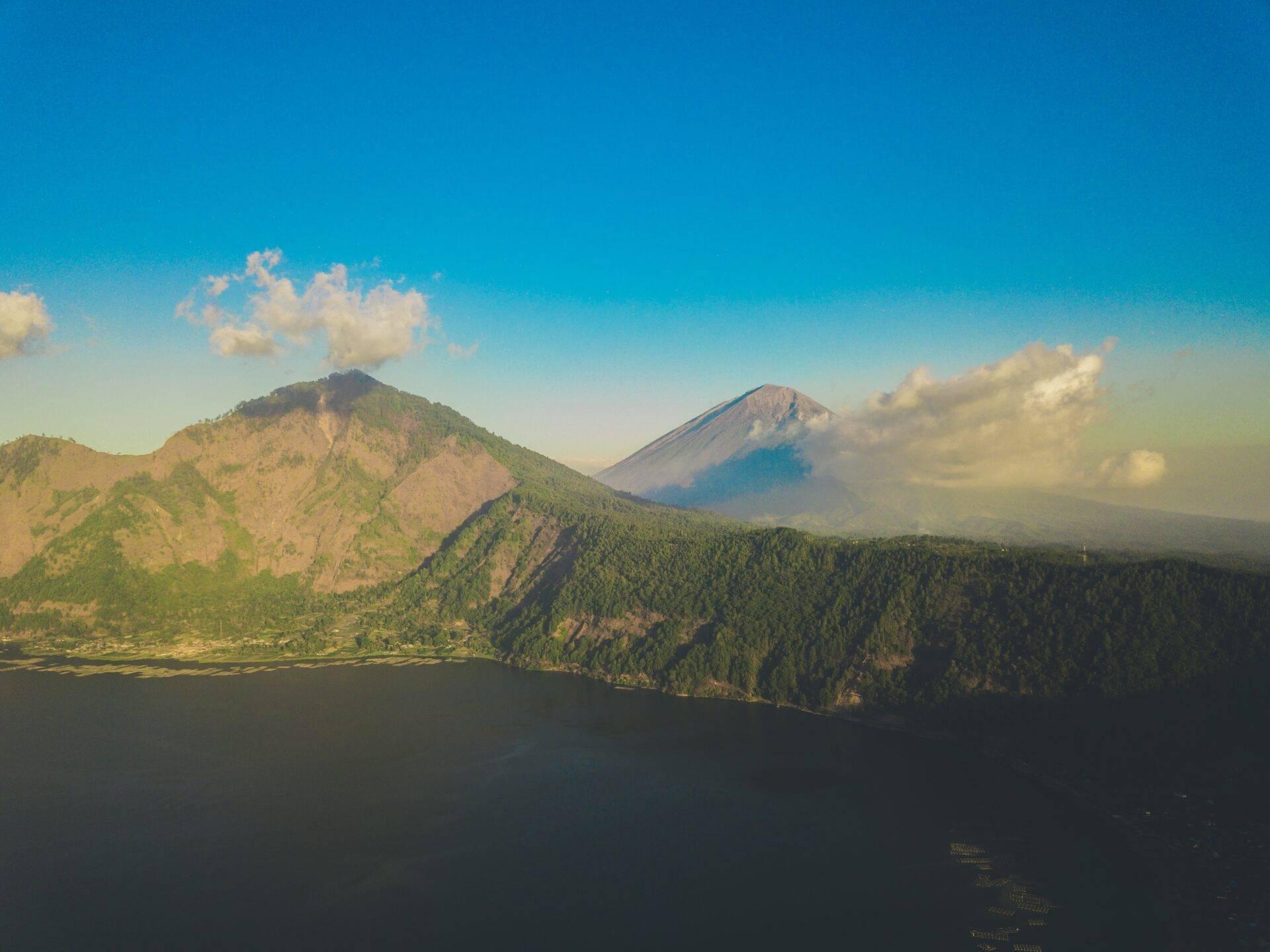 Deux volcans boisés se dressent au-dessus d’un lac calme sous un ciel bleu dégagé