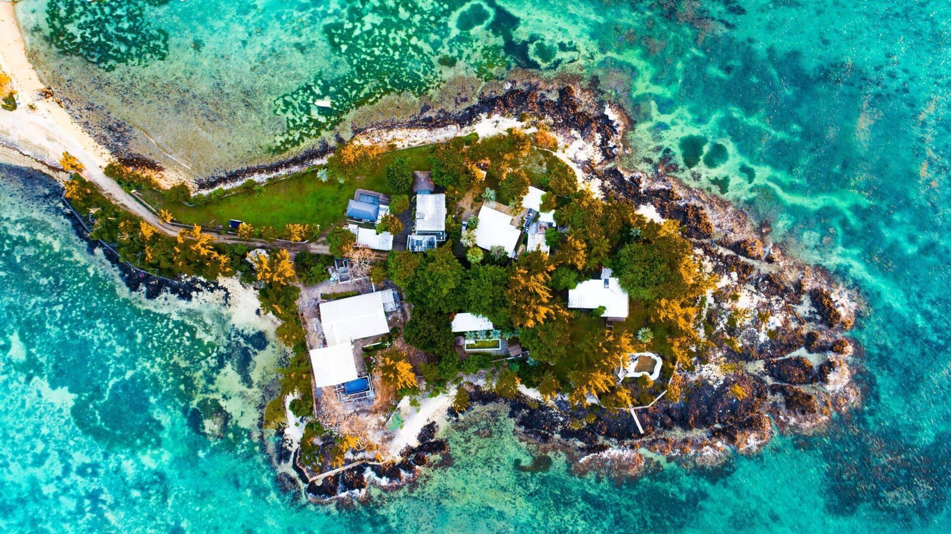 Vue aérienne d’une petite île rocheuse avec maisons blanches, végétation verte et eaux turquoise cristallines