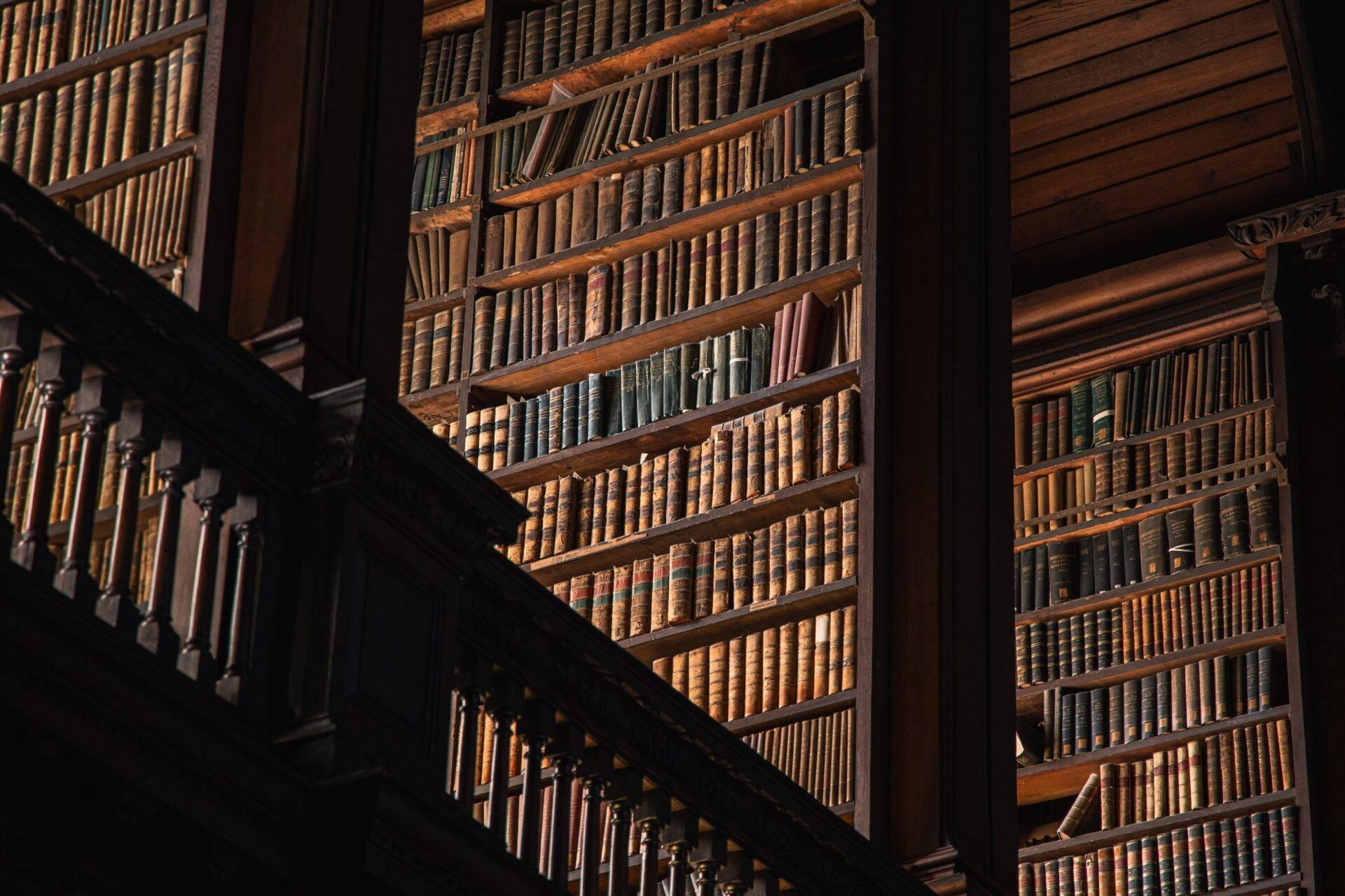Intérieur de bibliothèque historique avec rayonnages en bois remplis de livres anciens, escalier en bois et éclairage naturel